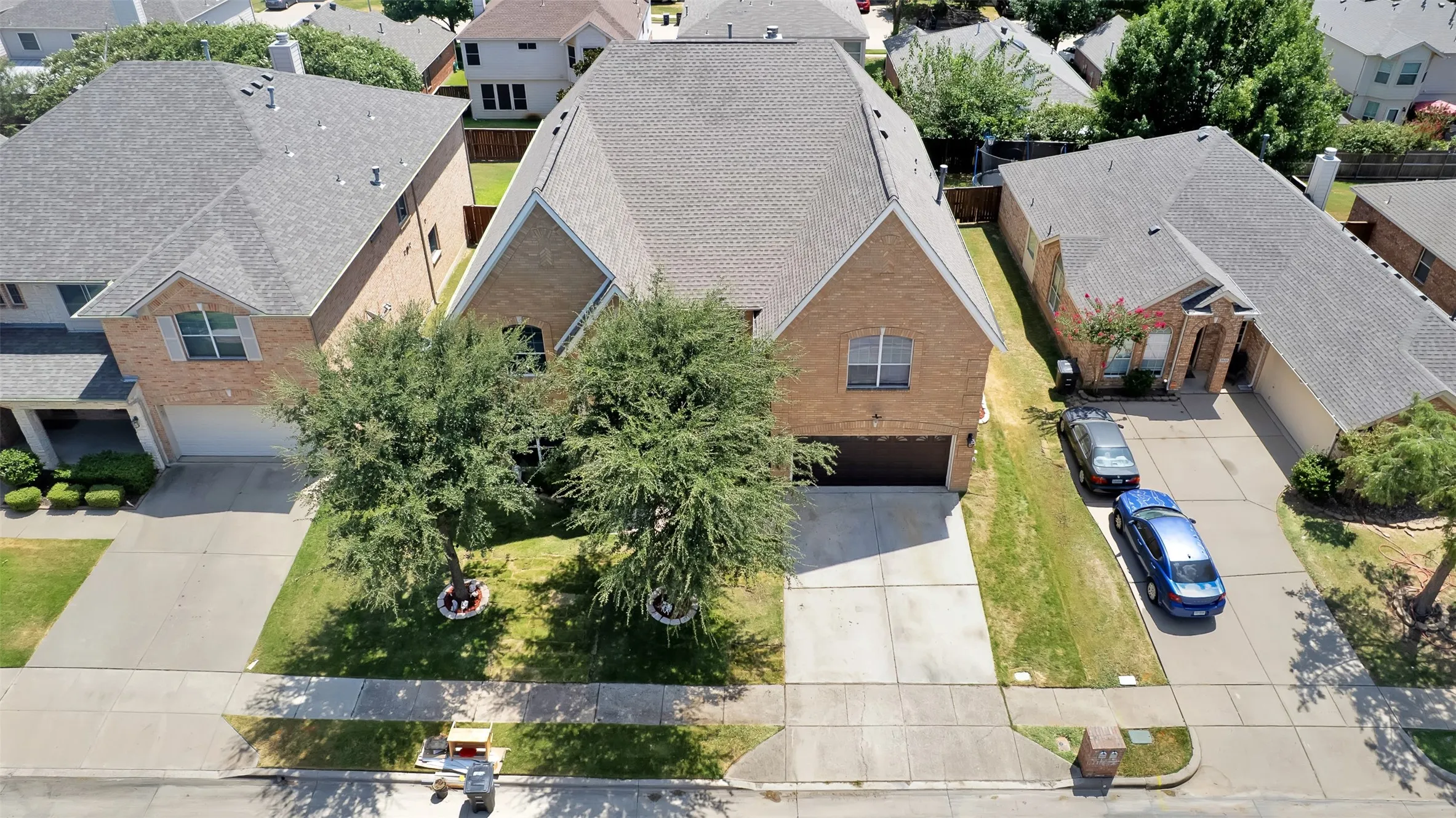 Brick exterior with an attached garage, paved driveway, and mature landscaping