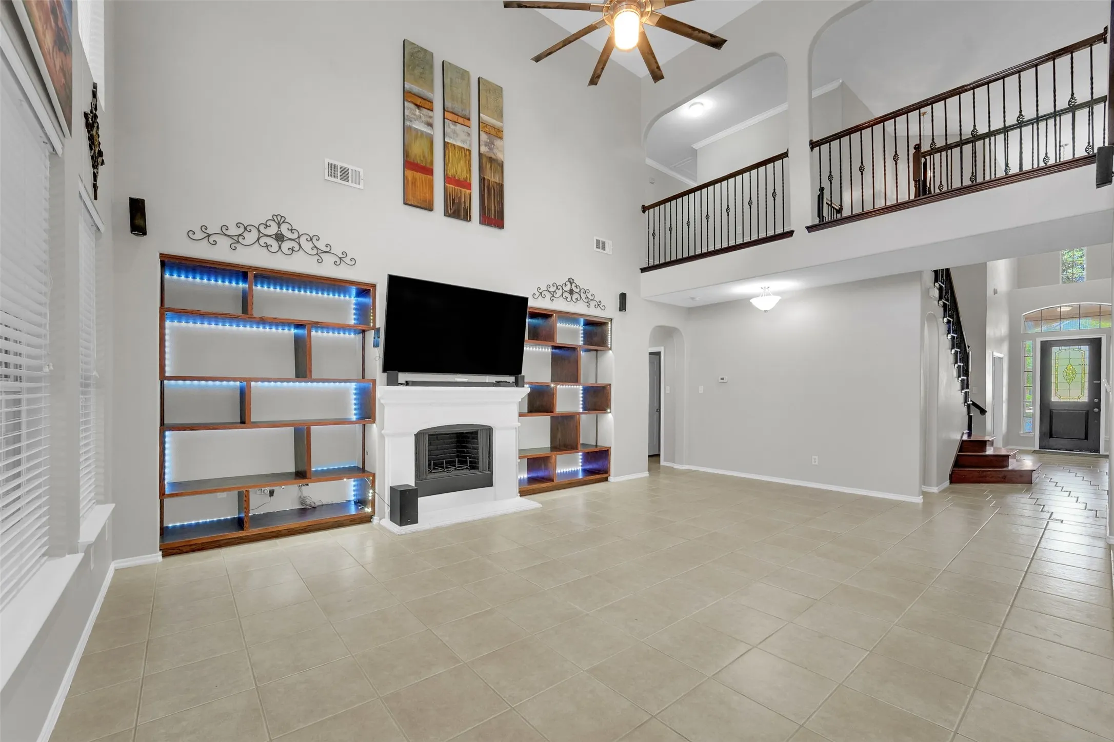 Two-story living area with high ceilings, a gas fireplace, built-in shelving with accent lighting, and tile flooring