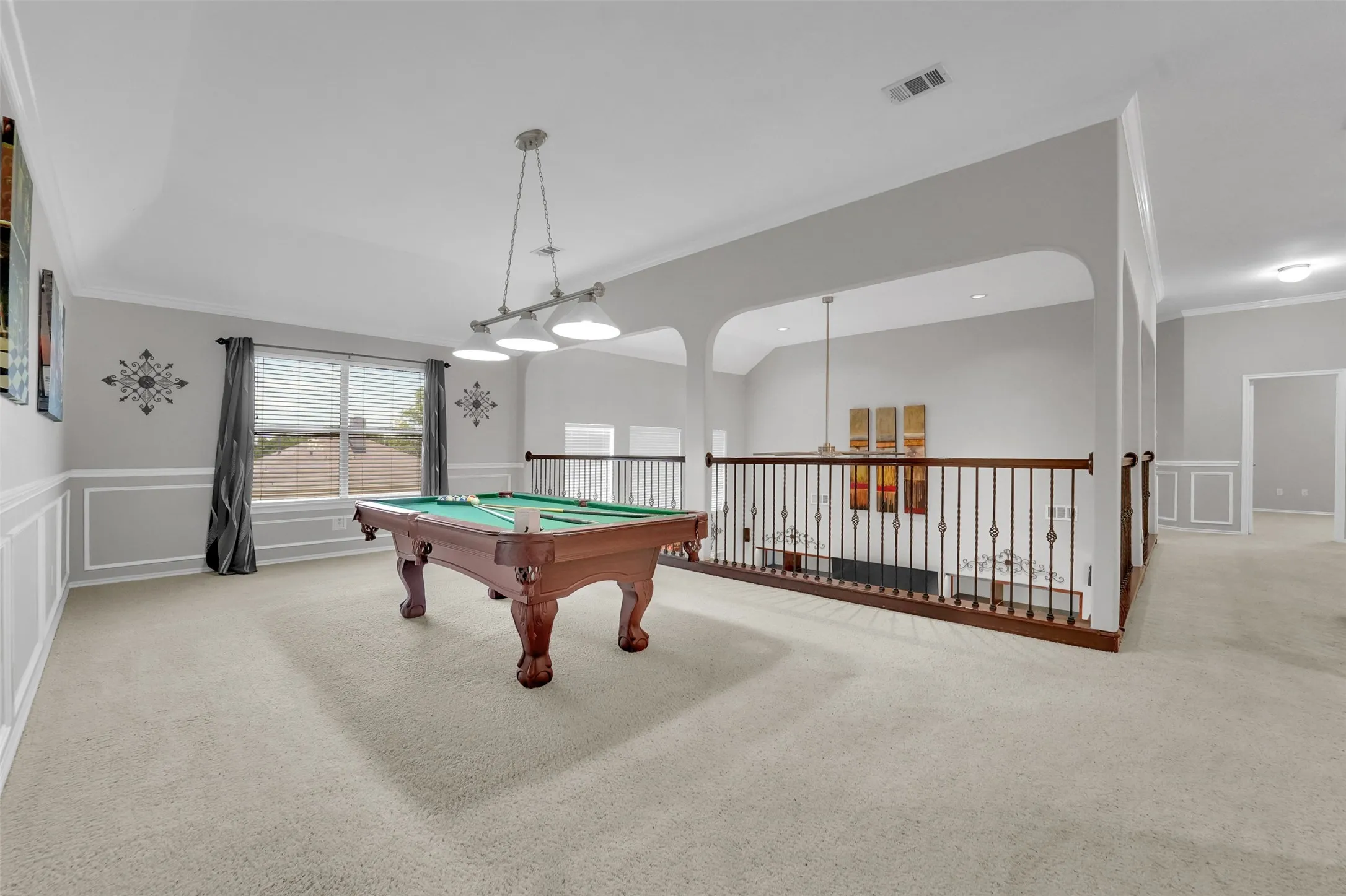 Spacious loft area featuring light-colored carpeting, wainscoting with decorative trim, and a window with blinds