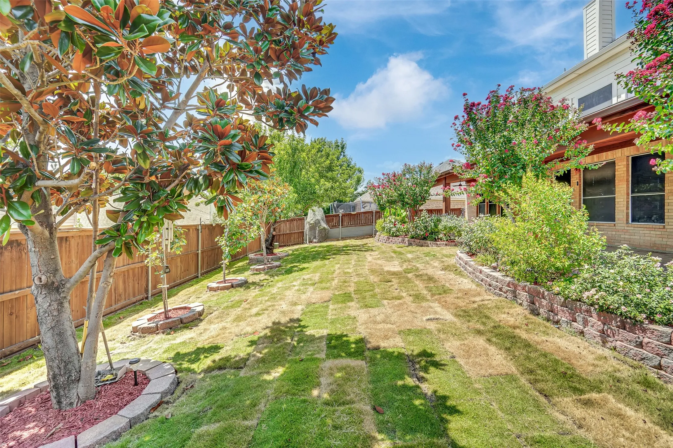Expansive backyard featuring a manicured lawn, established trees, and a privacy fence