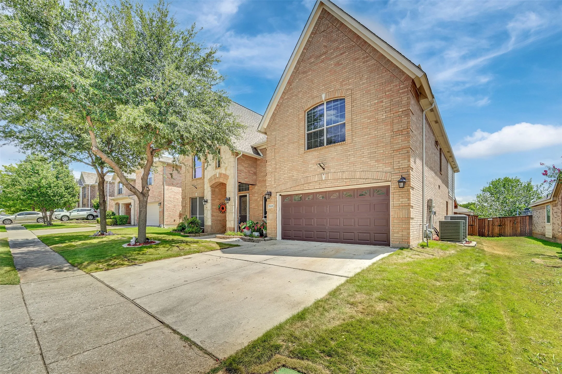 Brick exterior with stone accents, arched entryway, attached garage, concrete driveway, and mature trees