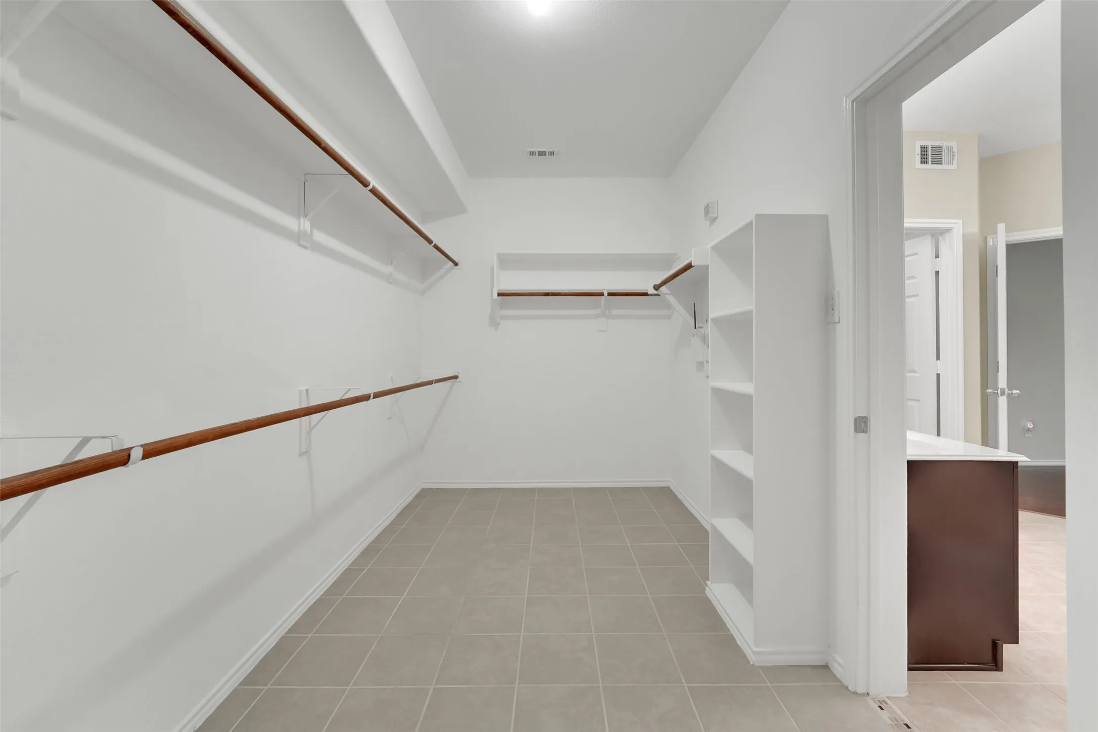 Spacious closet featuring tiled flooring, built-in shelving, and multiple hanging rods