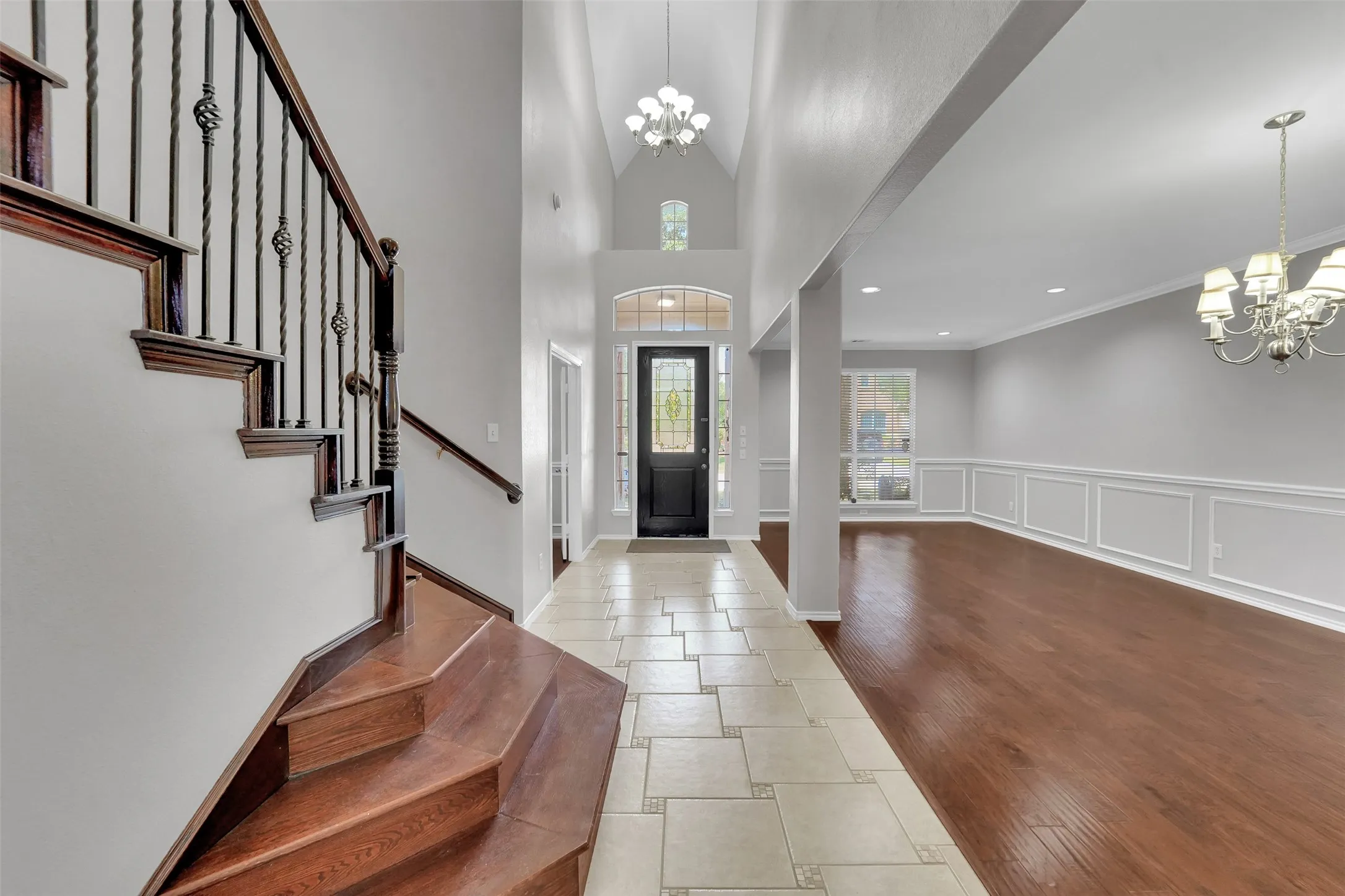 Two-story foyer with tile flooring, wood staircase with wrought iron spindles, high ceilings, and a formal dining room with wood-finish flooring and wainscoting