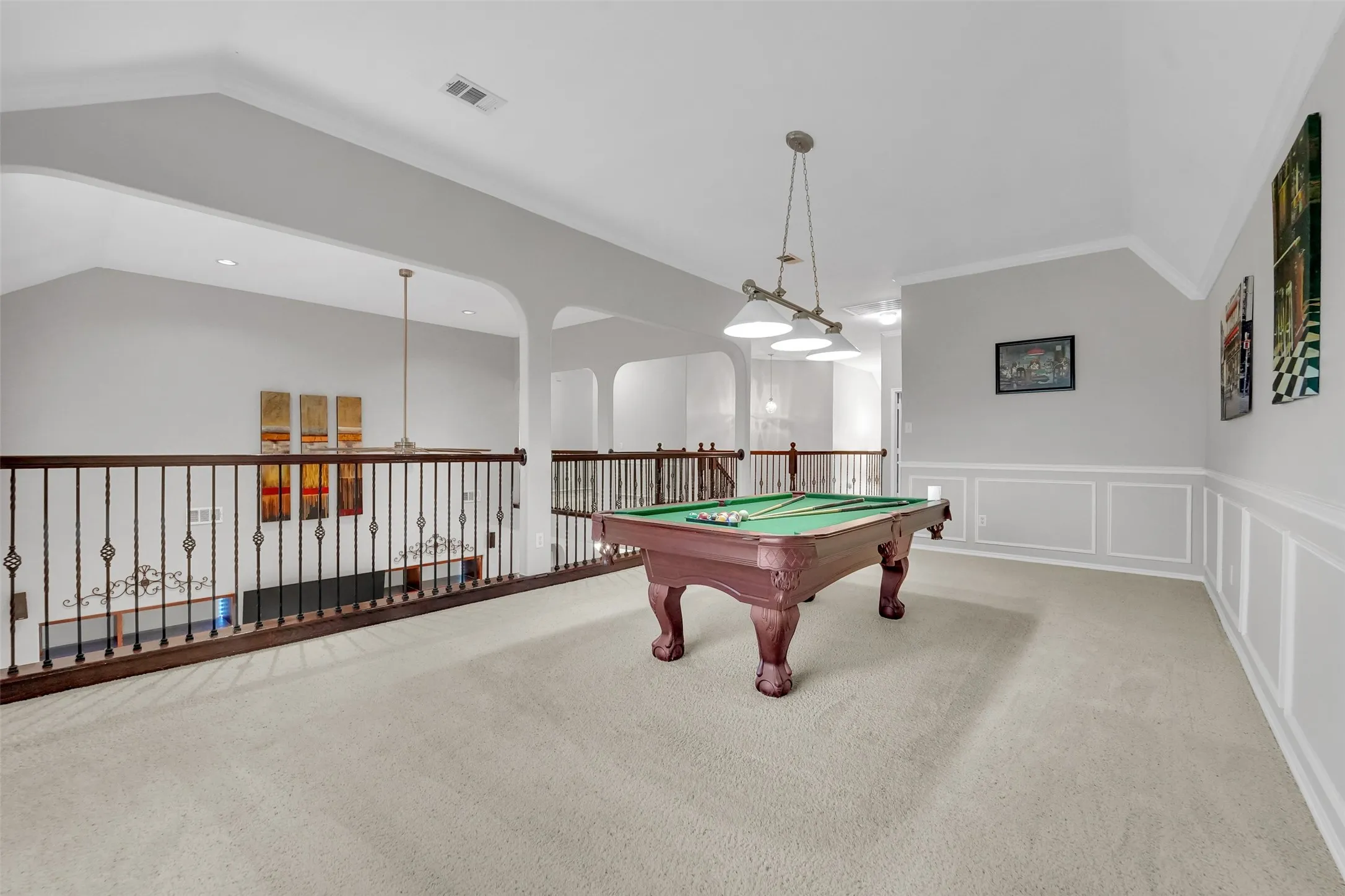 Open loft area with vaulted ceiling, carpeted flooring, wainscoting, and decorative iron balusters