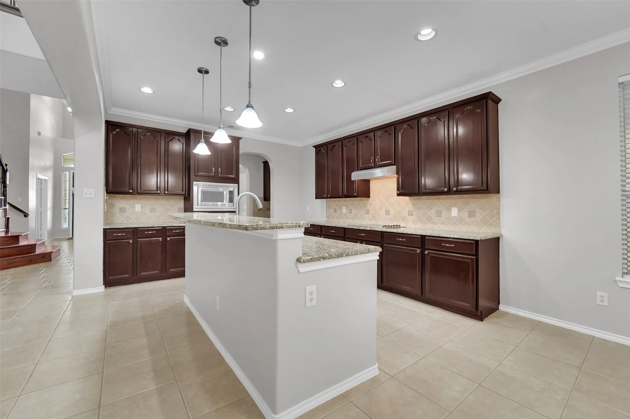 Kitchen featuring rich wood-finish cabinetry, granite countertops, a tiled backsplash, and recessed lighting