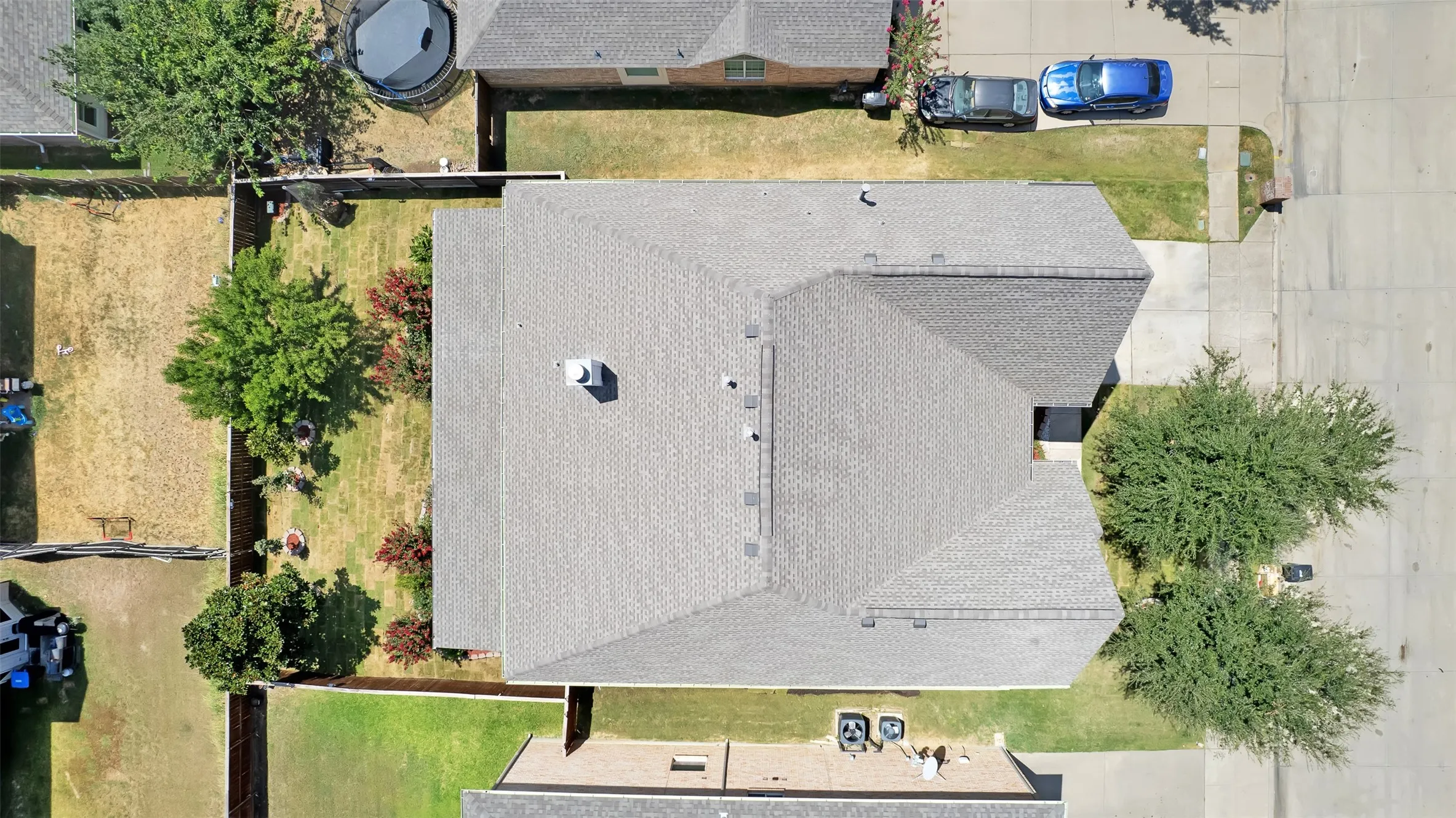 Gabled roof with a central chimney, mature landscaping, fenced rear yard, concrete driveway, and concrete sidewalk