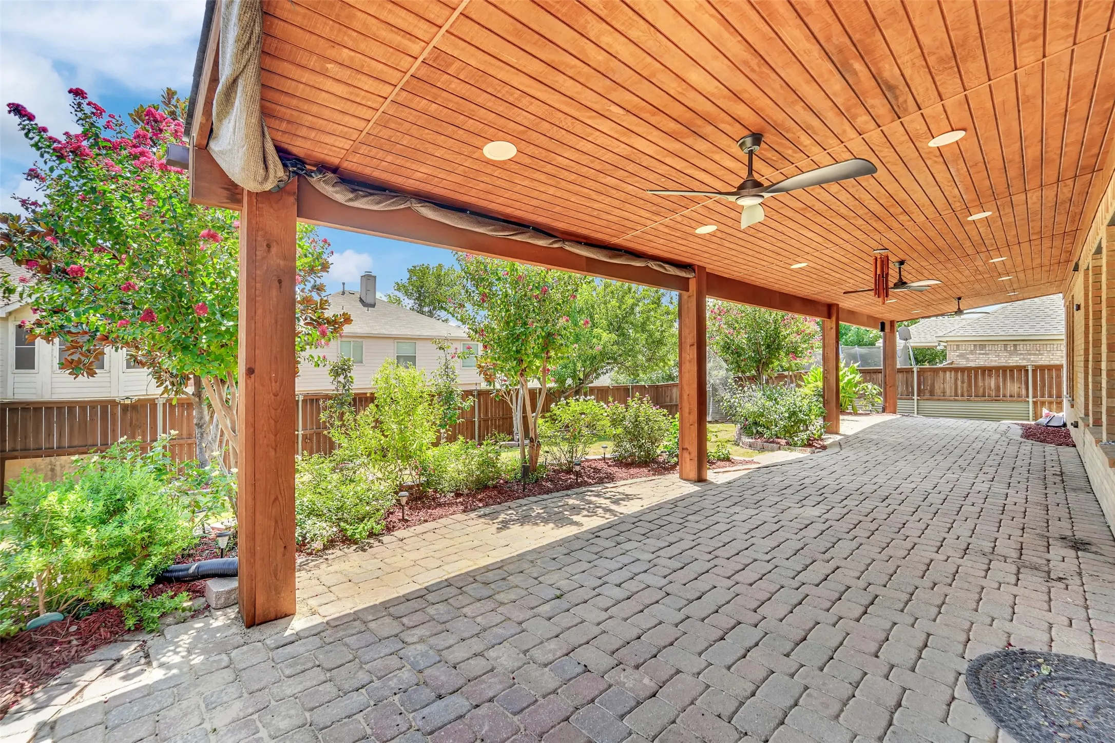Expansive covered patio featuring a wood-panel ceiling, recessed lighting, ceiling fans, and paver flooring