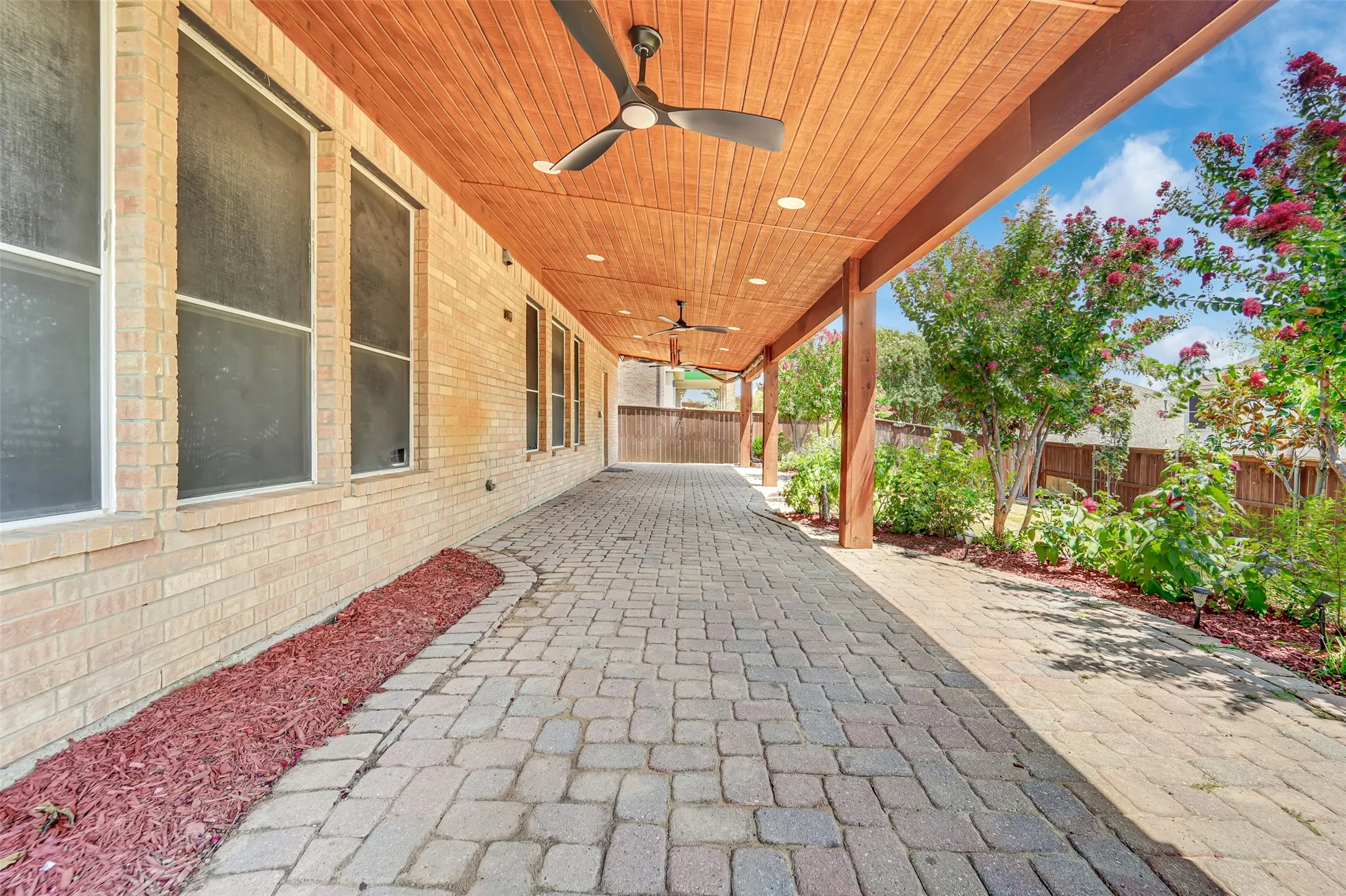 Expansive brick paver patio featuring a wood-panel ceiling with integrated ceiling fans and recessed lighting, supported by timber posts