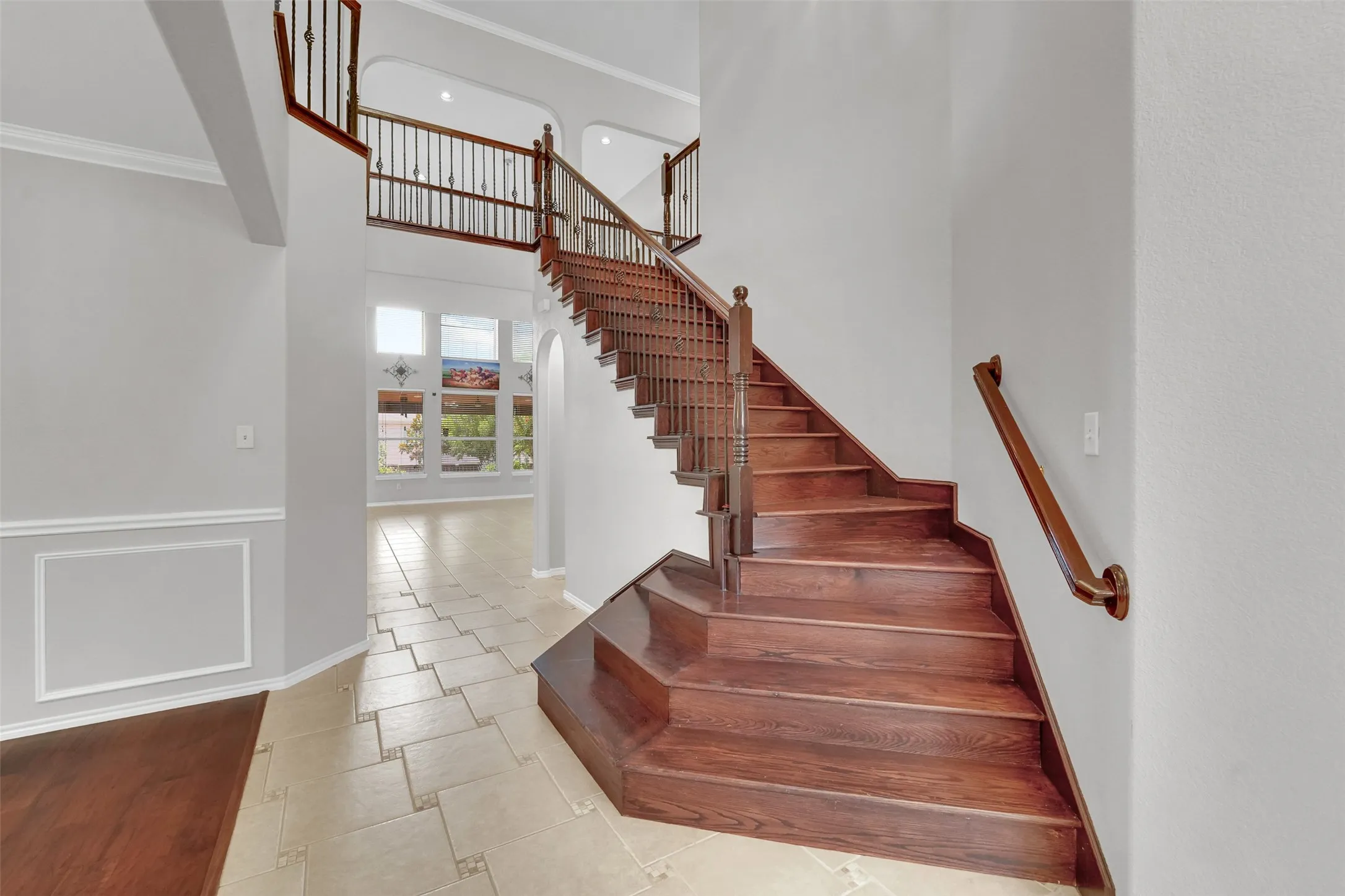 Wood-finish staircase with wrought iron balusters, tiled flooring, wainscoting, and large windows with arched transoms