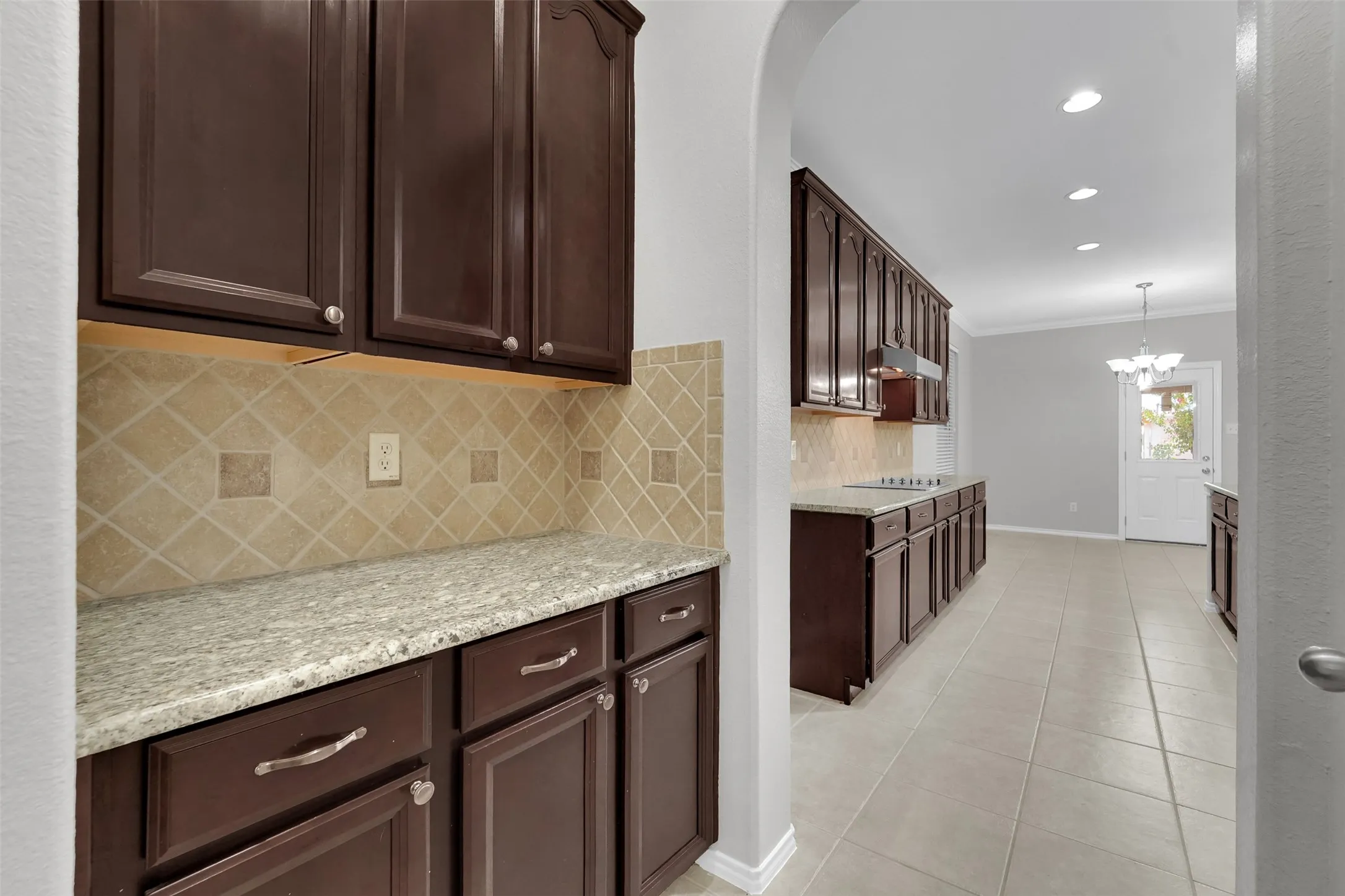 Dark wood-finish cabinetry with silver-tone hardware, light speckled countertops, and a tiled backsplash