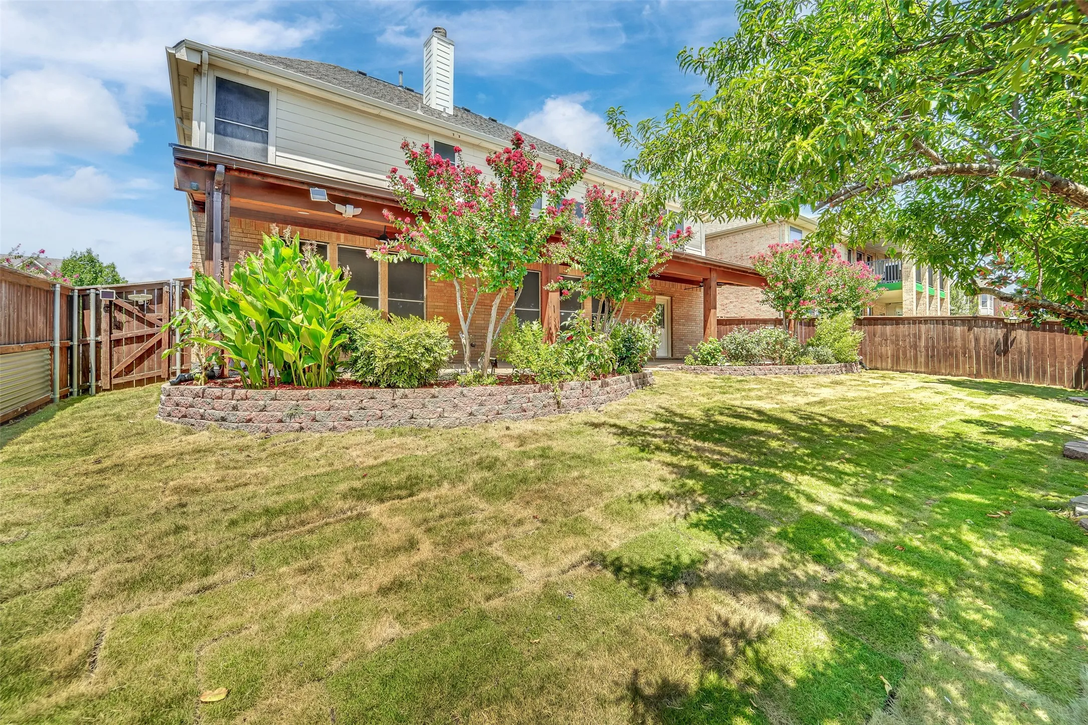 Expansive backyard featuring a manicured lawn, brick retaining wall, and mature trees