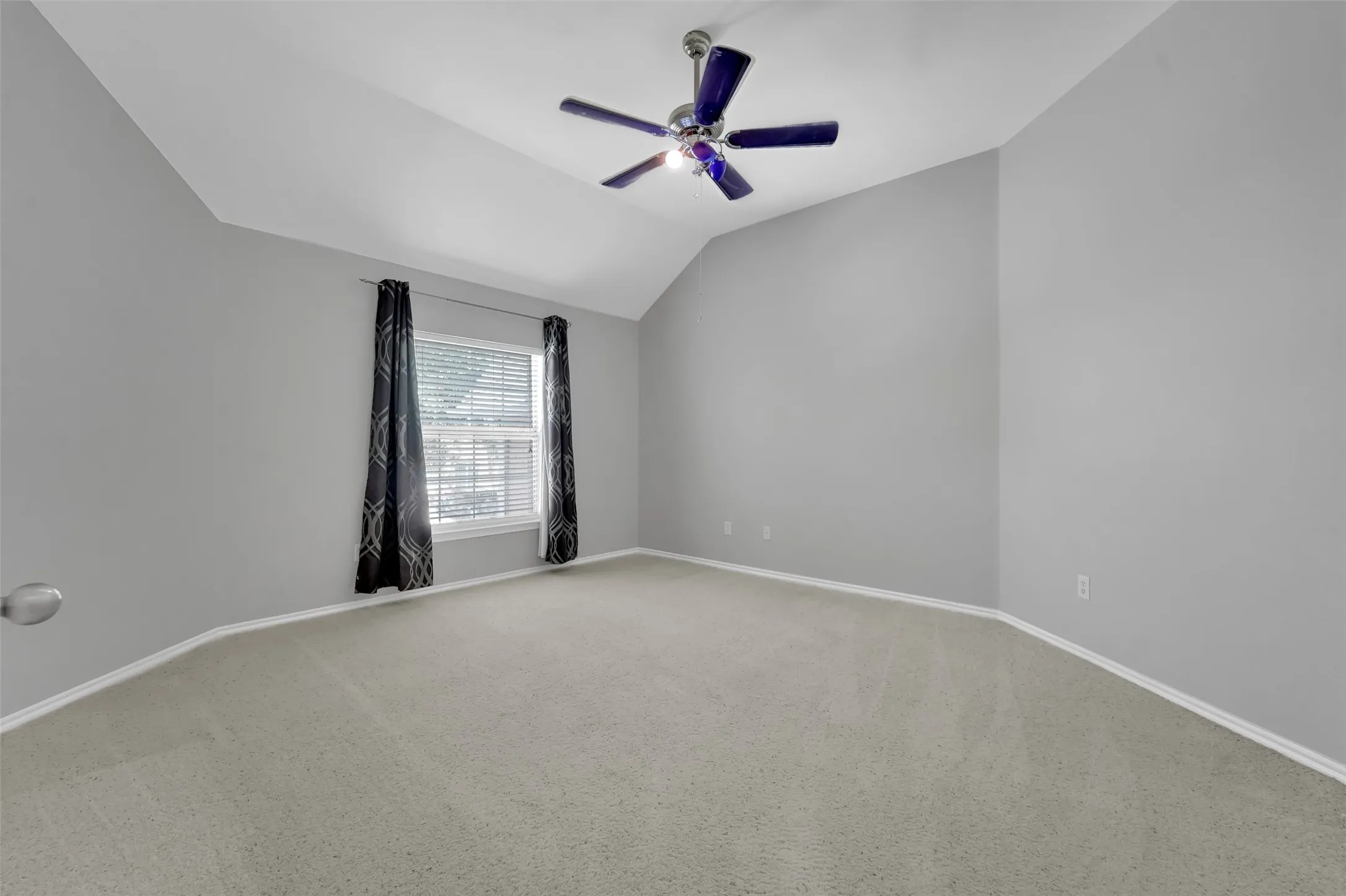 Vaulted ceiling with a ceiling fan, light-toned carpeting, and a window with blinds