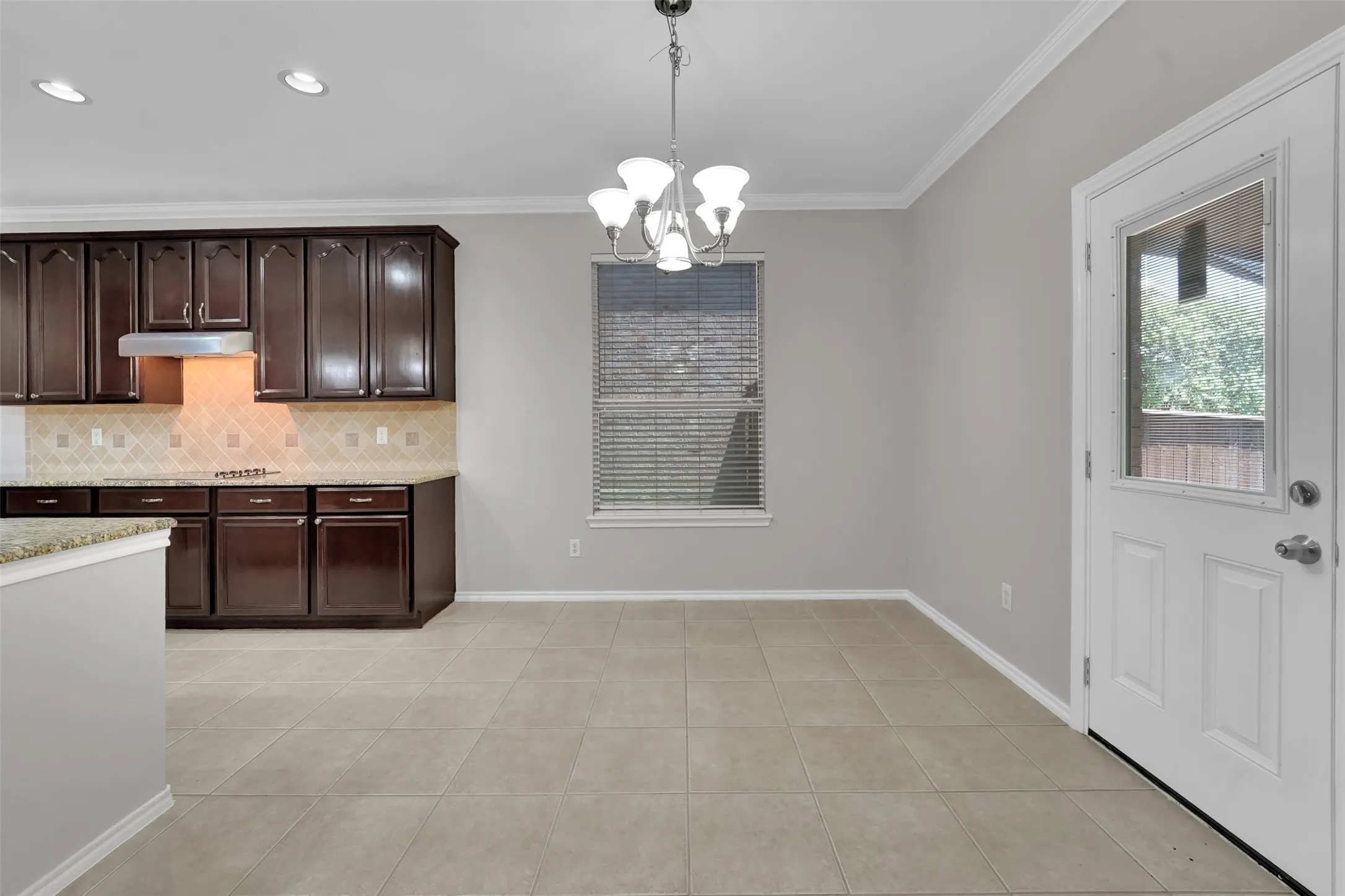 Dark wood cabinetry, tiled backsplash, recessed lighting, and a chandelier illuminate the dining space