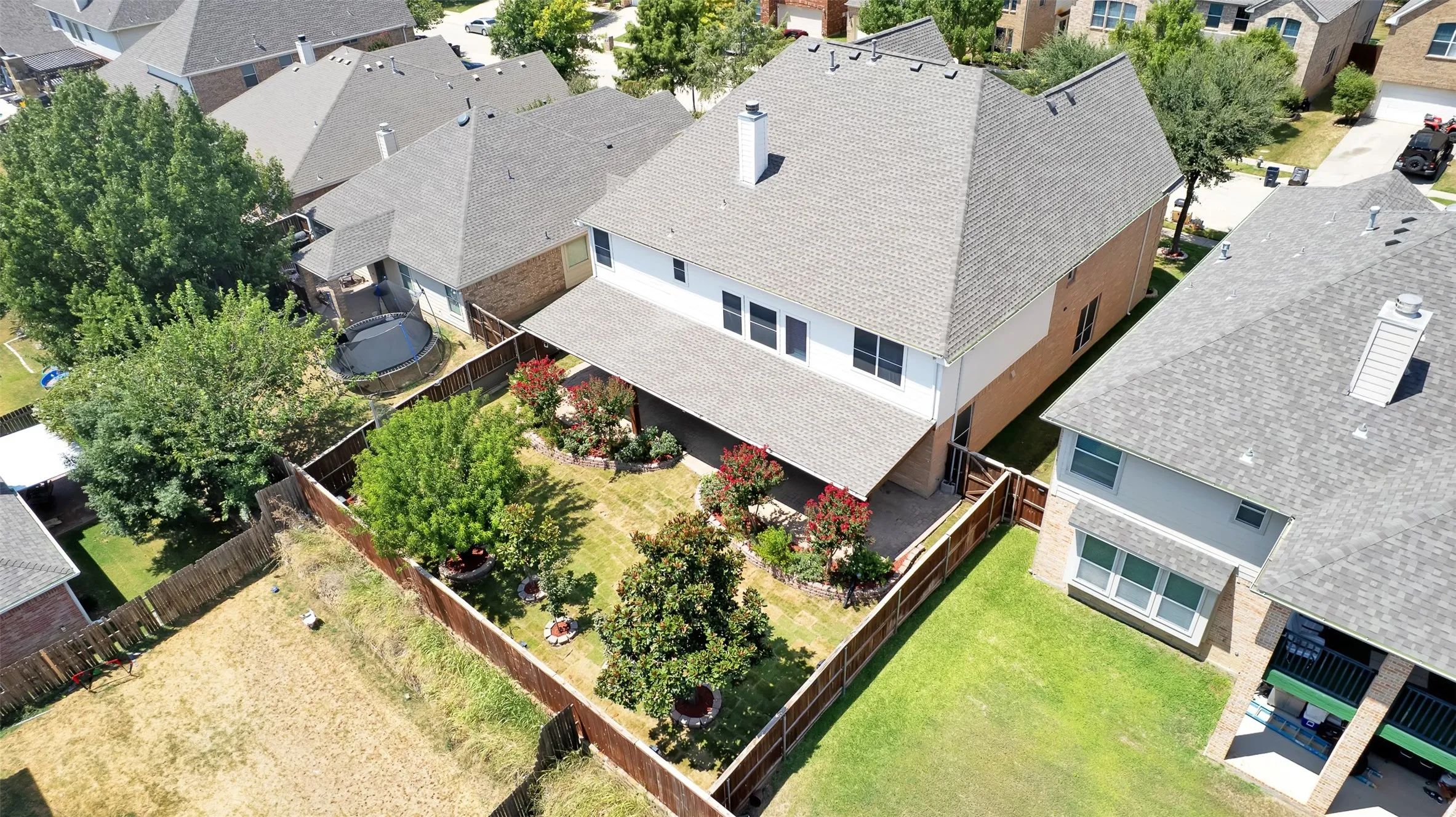 Expansive backyard with a manicured lawn, established landscaping beds, mature trees, and a wooden privacy fence