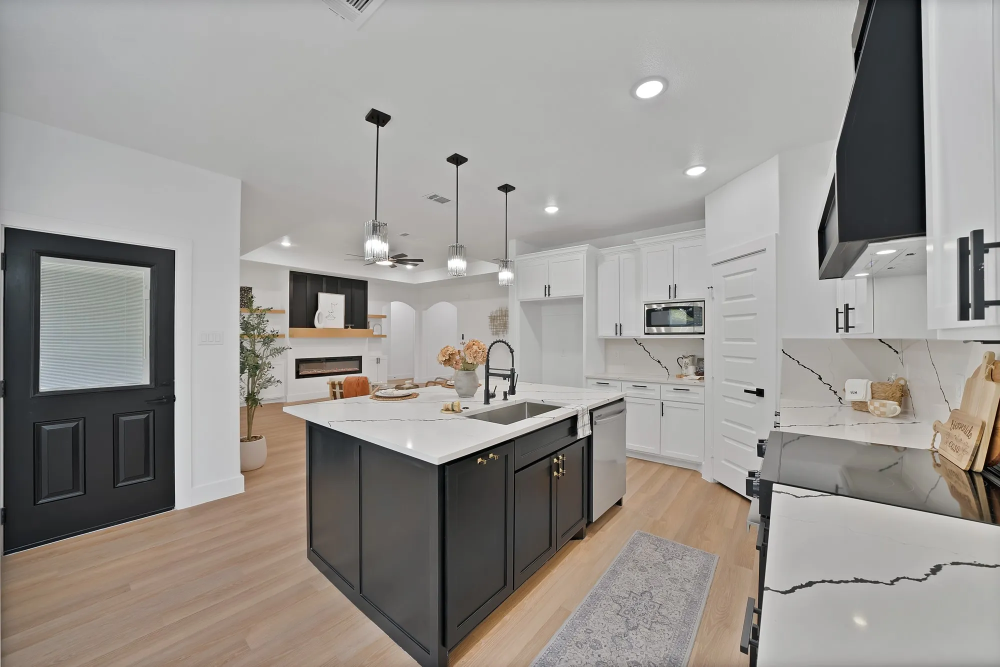 Kitchen with a dark cabinet island, stainless steel sink, white countertops, and light wood-finish flooring