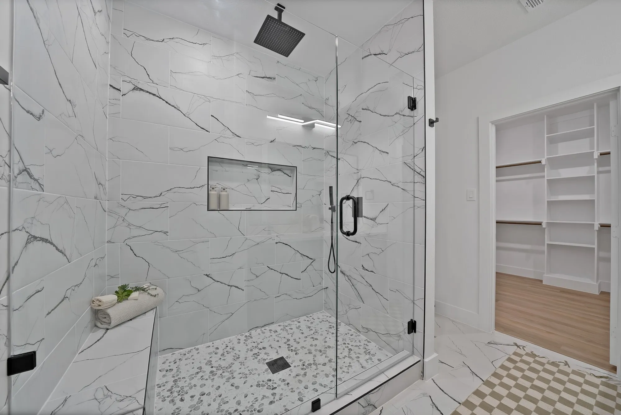 Walk-in shower with clear glass enclosure, rainfall showerhead, tiled bench, and recessed niche