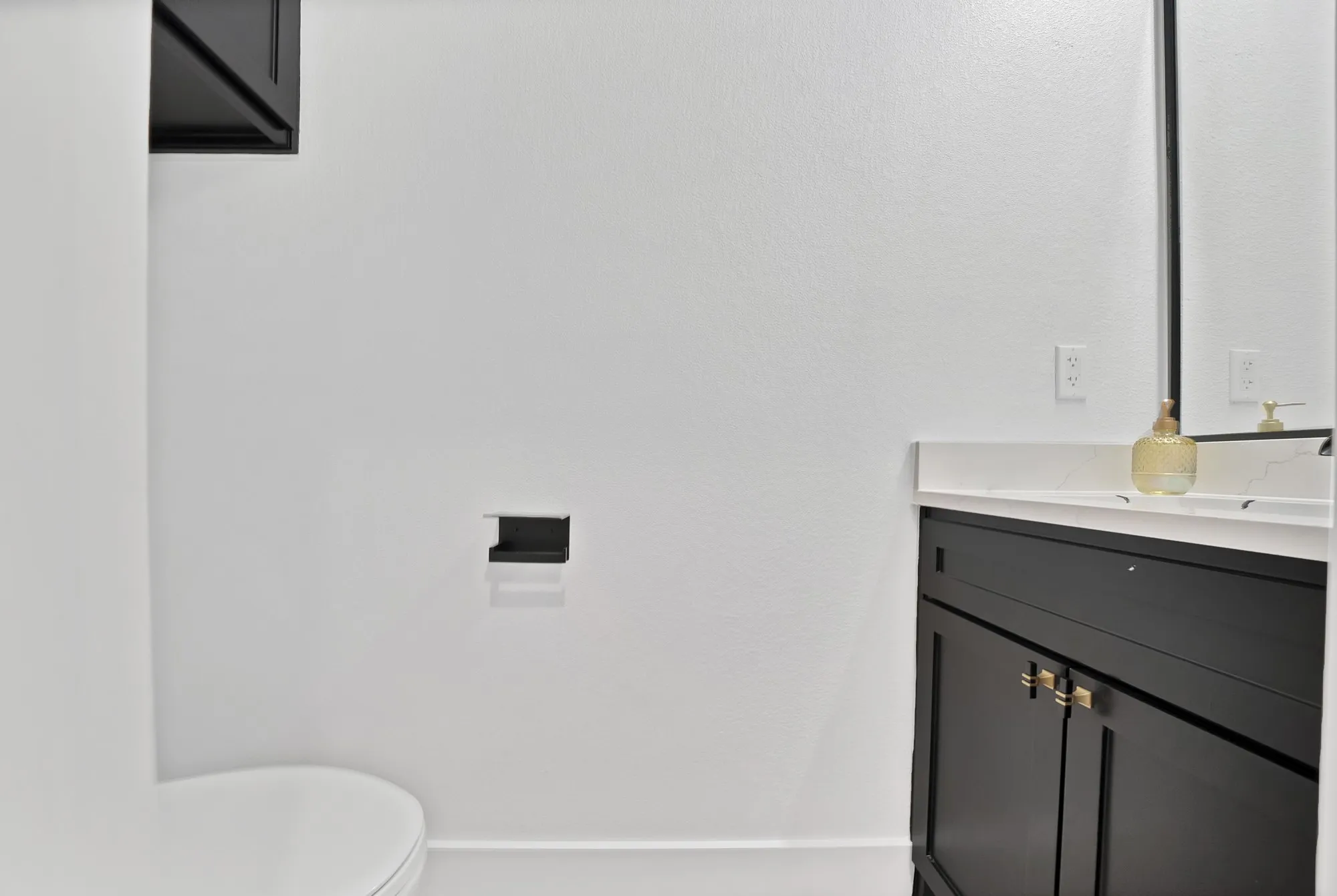 Black vanity with gold-finish hardware, a white countertop, and a framed mirror