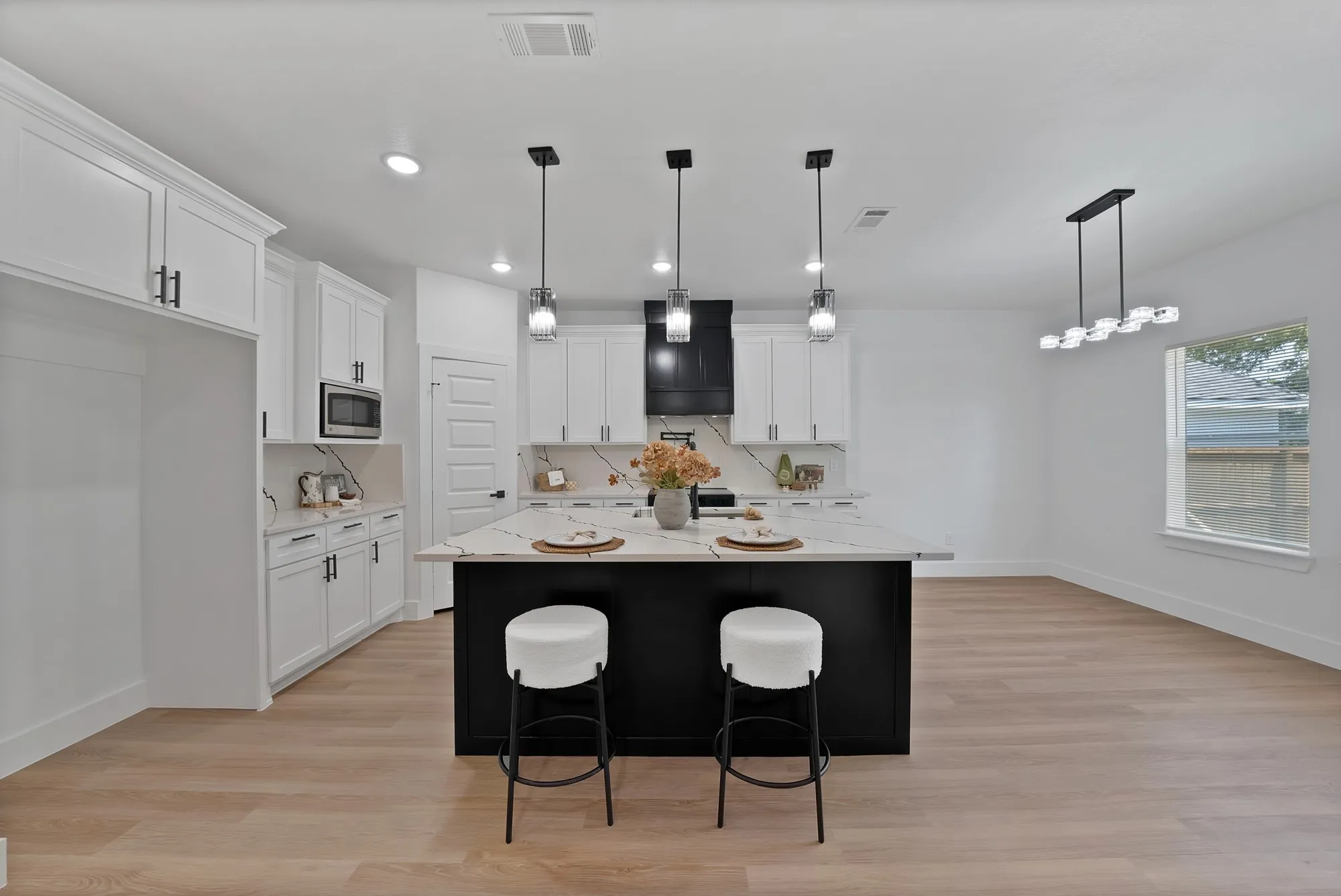 Kitchen featuring a large island with a stone-finish countertop, white cabinetry, a black range hood, and wood-finish flooring
