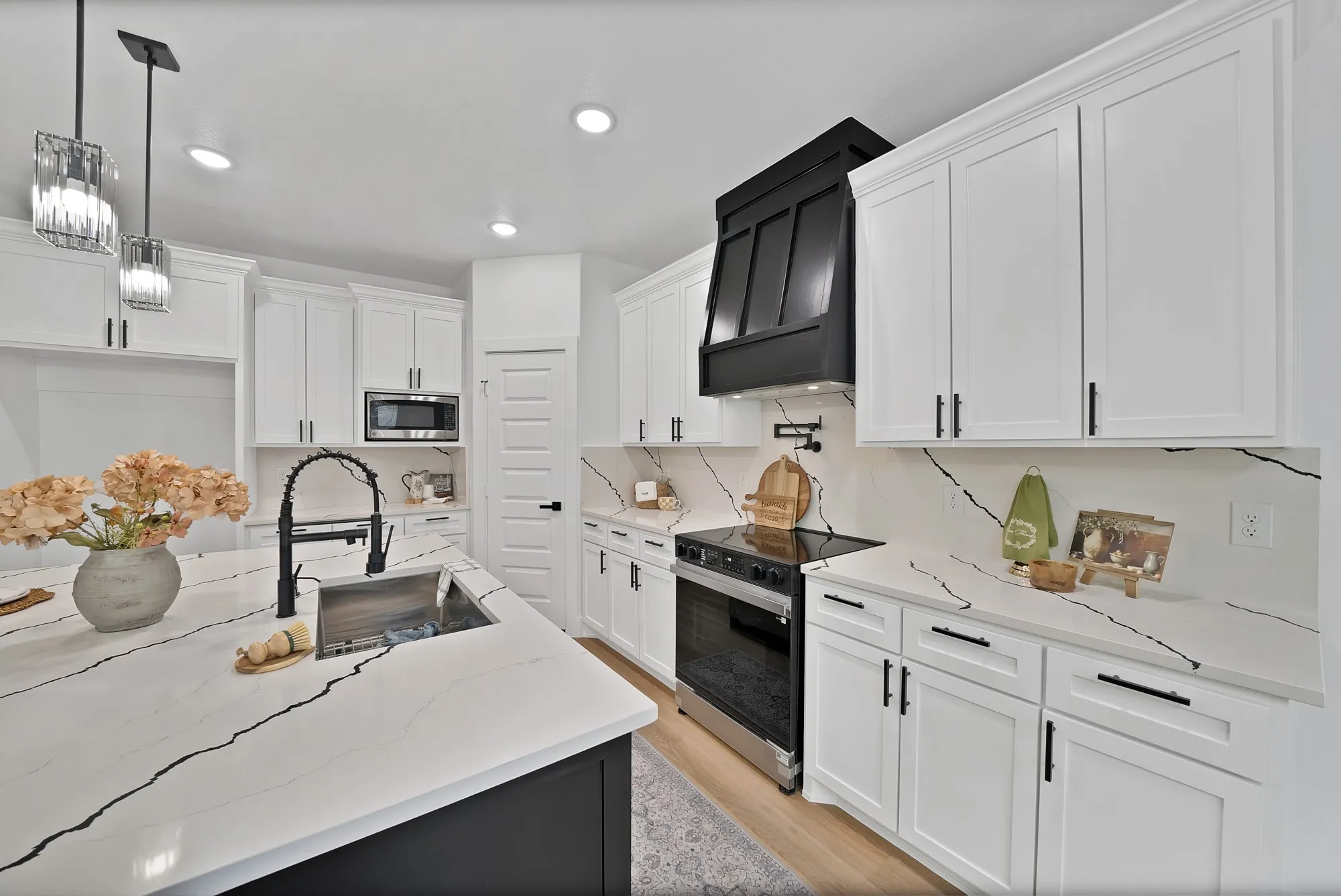 Kitchen featuring a large island with an undermount sink, white cabinetry, integrated stainless steel appliances, a black range hood, and light wood-finish flooring