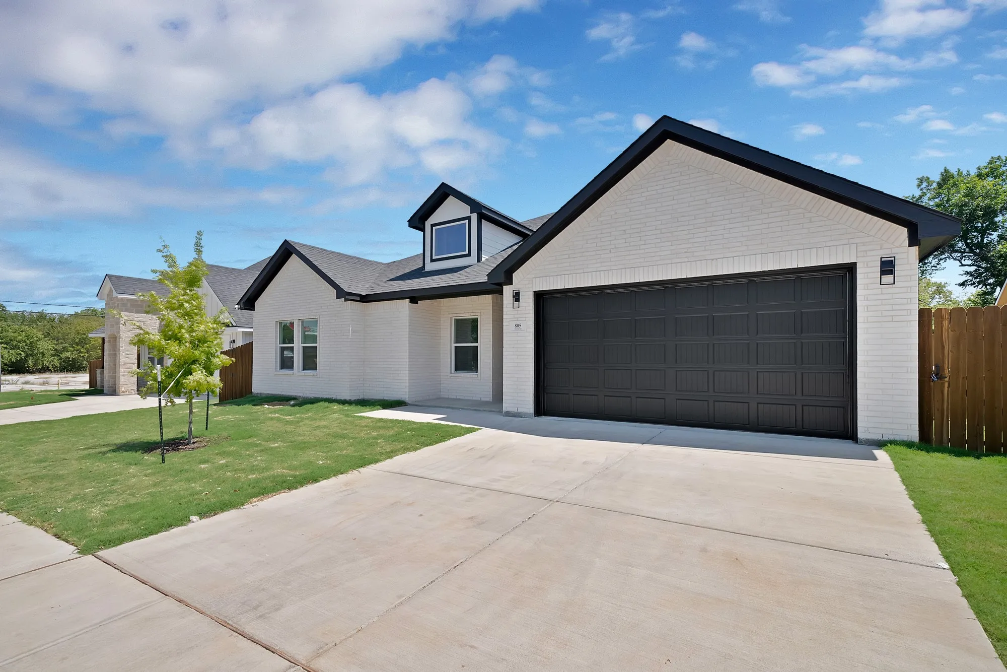 White brick exterior with a dark shingle roof and a black garage door