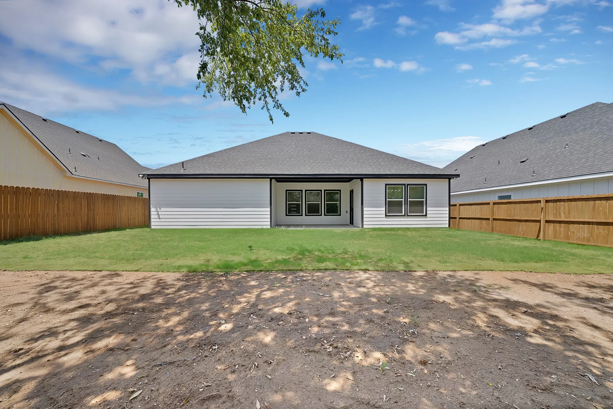 Rear exterior featuring white siding, a covered patio, multiple windows with black trim, a gray shingle roof, and a wood fence