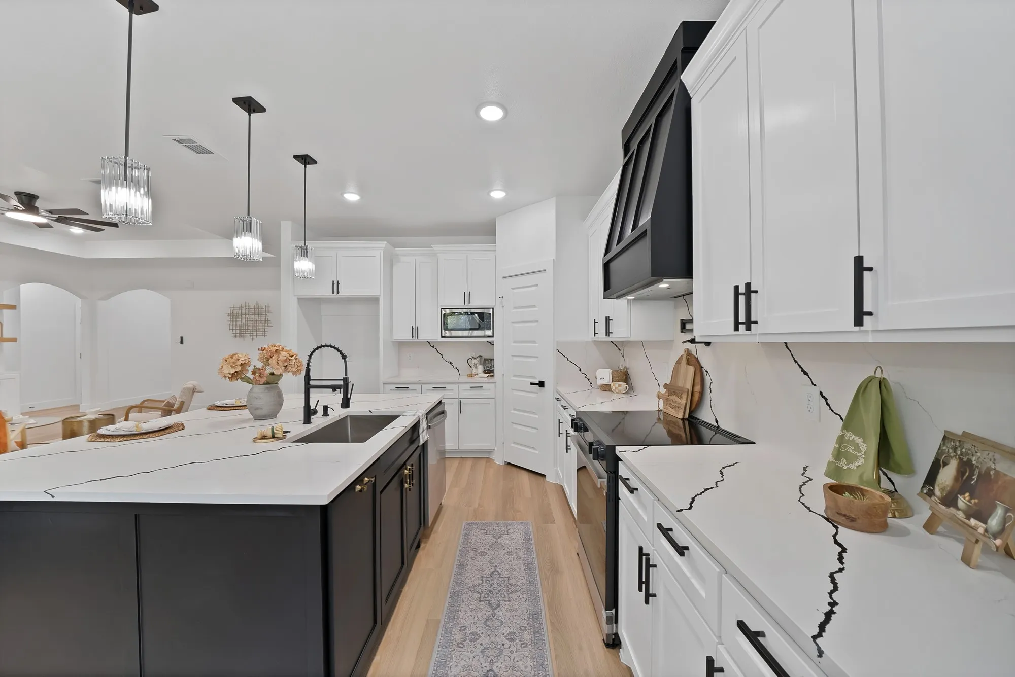 Kitchen featuring white cabinetry with black hardware, an expansive island with an undermount sink, light wood-finish flooring, and white countertops with dark veining
