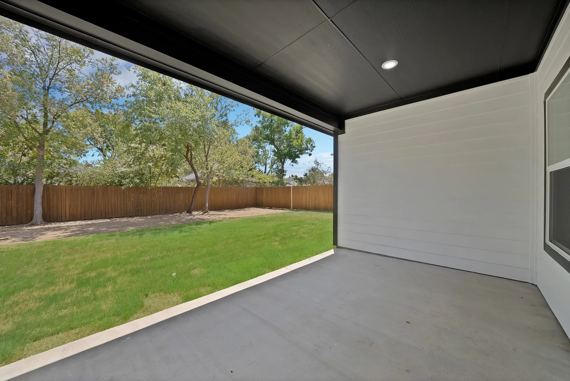 Covered patio with concrete flooring, recessed lighting, white siding, and a wood privacy fence