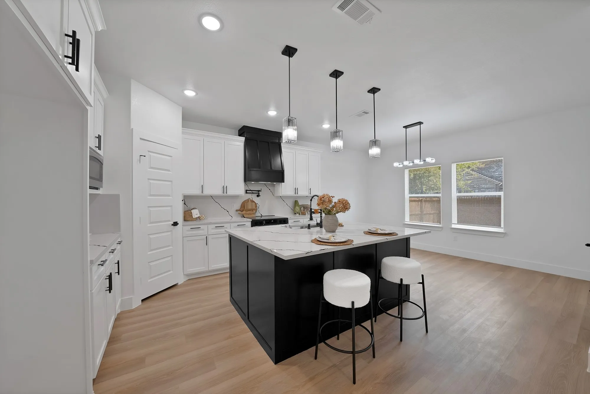 Spacious kitchen featuring a large black island with white countertop, white cabinetry, a black range hood, and wood-finish flooring
