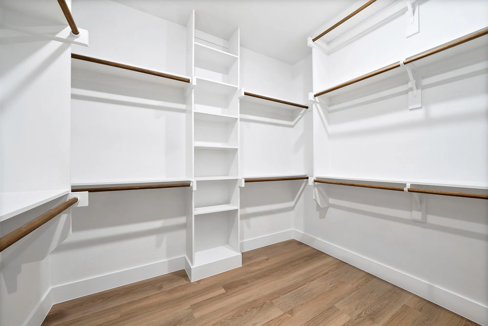 Custom closet system with built-in shelving, multiple hanging rods, and wood-finish flooring