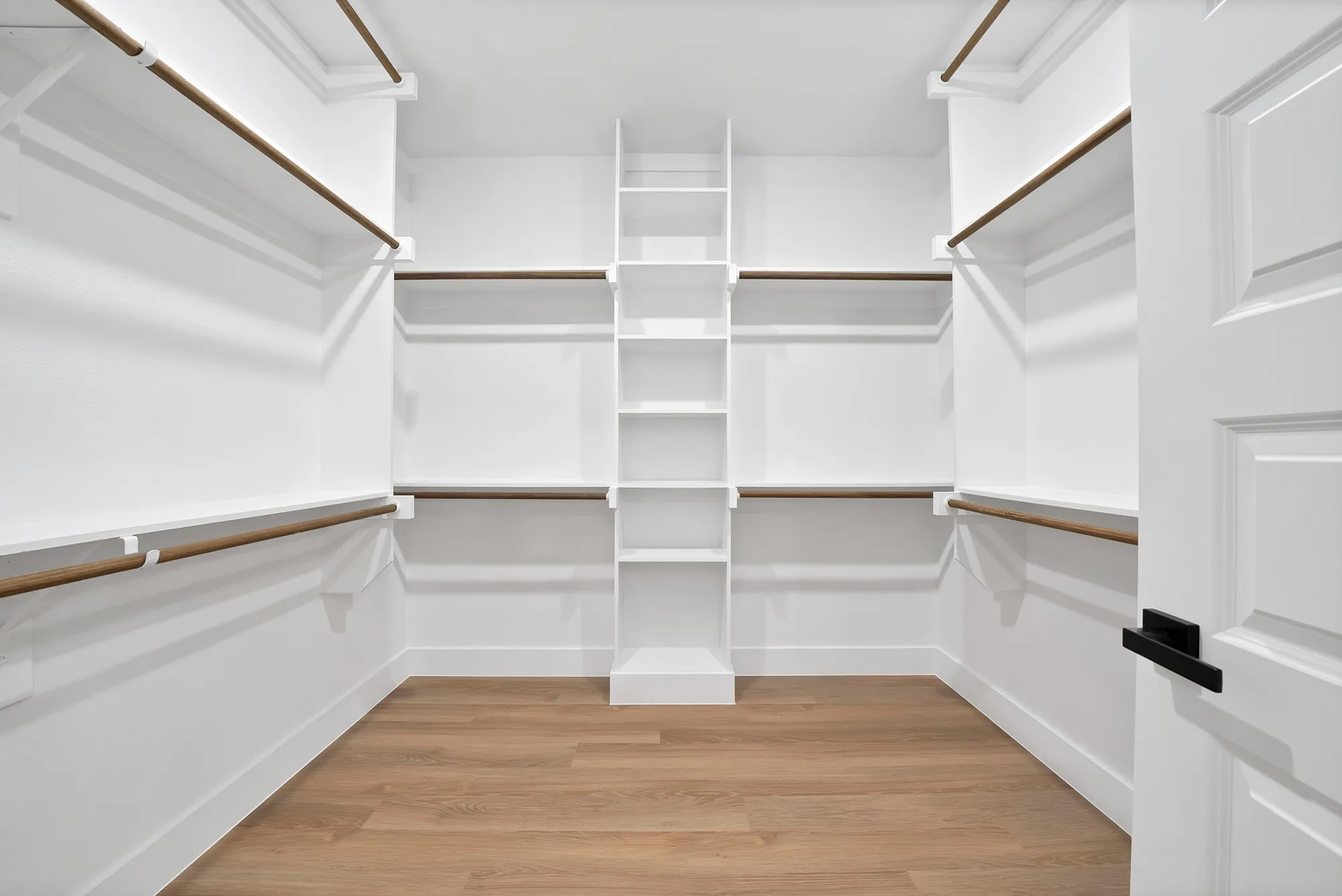 Walk-in closet with built-in shelving, hanging rods, and wood-finish flooring