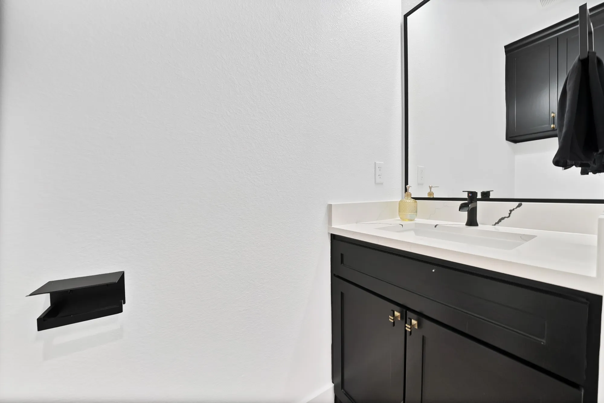 Built-in vanity with dark cabinetry, white countertop, integrated sink, and a black framed mirror