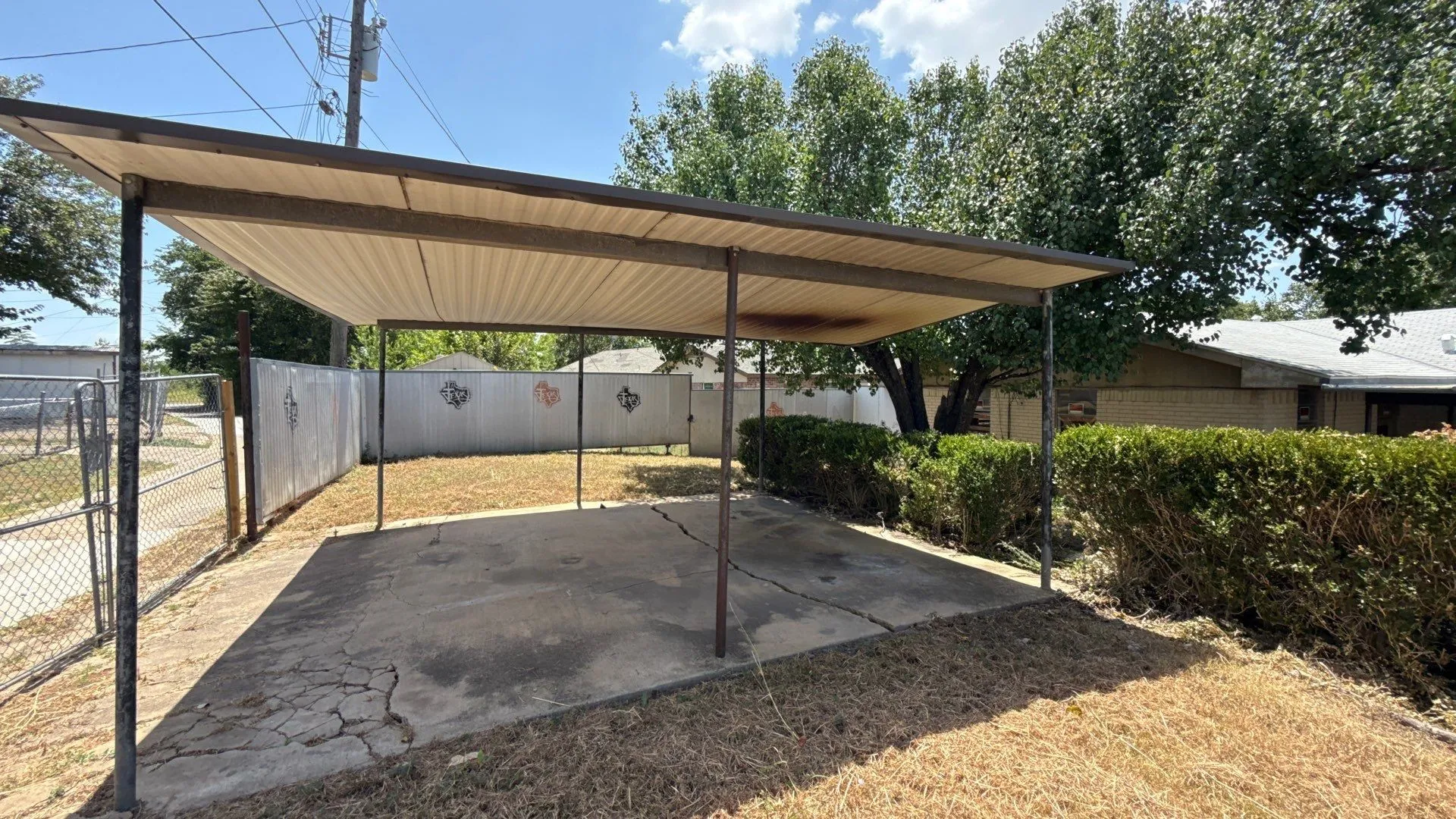 Carport with a corrugated roof, supported by metal posts, providing covered parking
