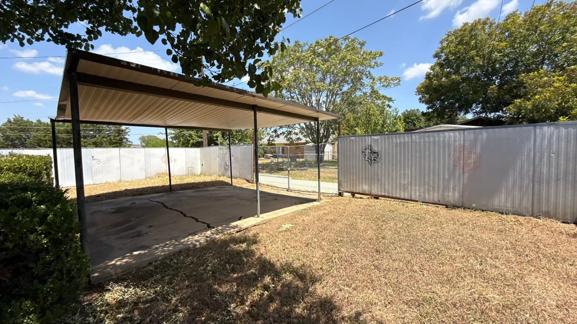 Carport structure with a concrete pad and corrugated metal fencing