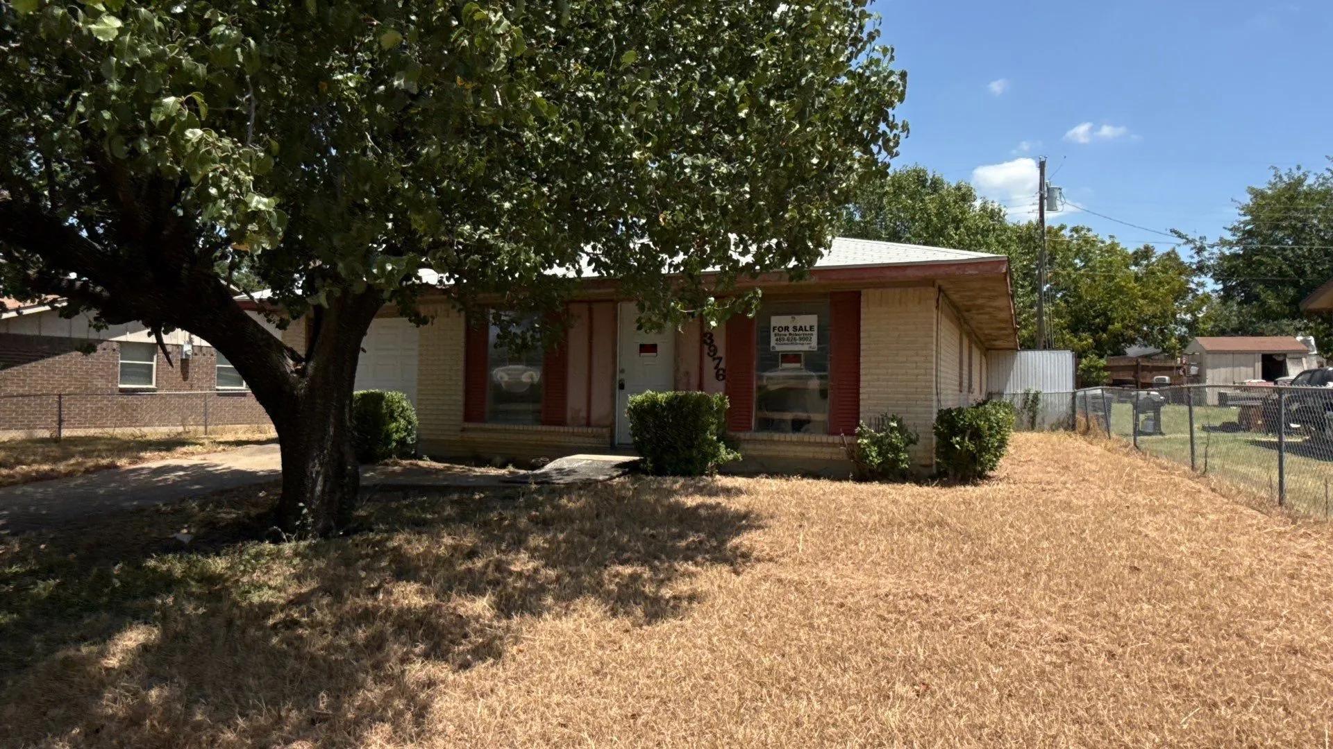 Brick exterior with a mature tree and a chain-link fence enclosing the yard