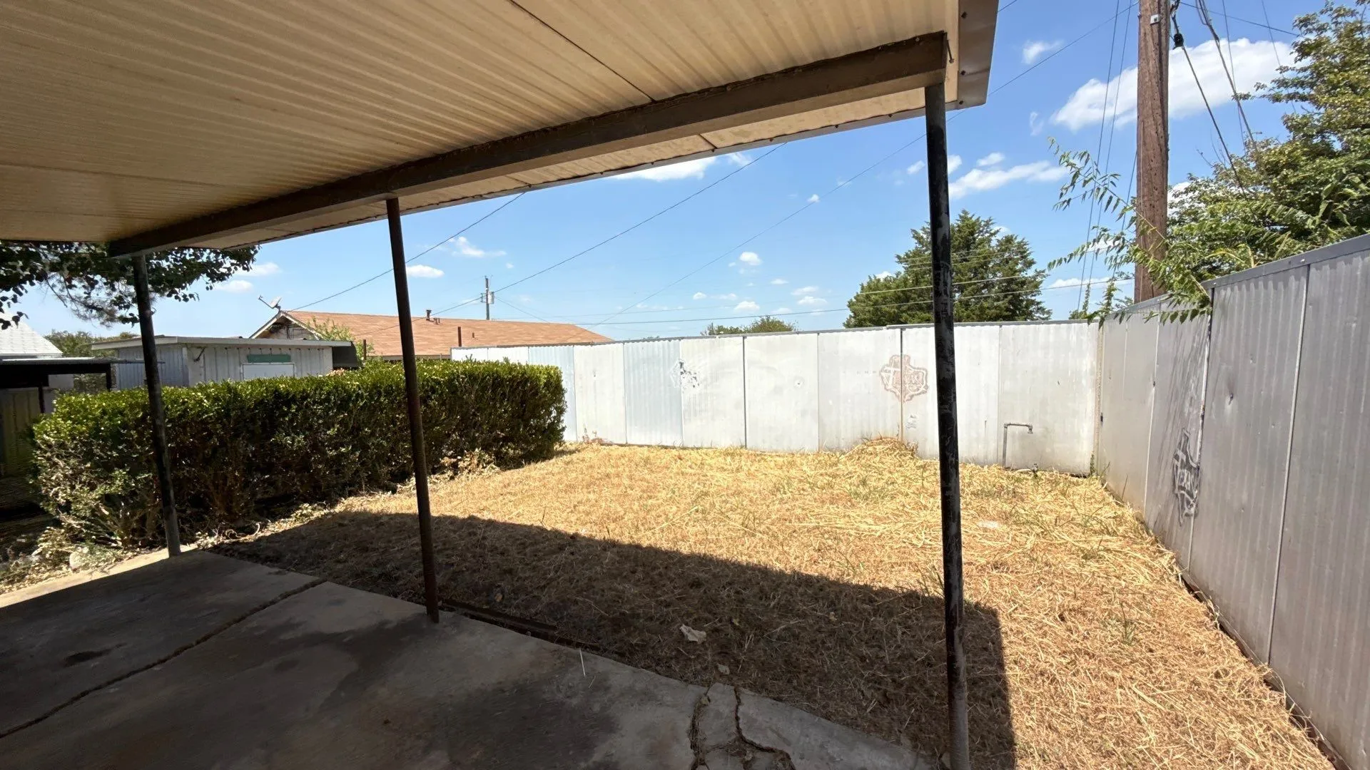 Outdoor covered patio with concrete flooring, supported by metal posts, leading to an open yard space