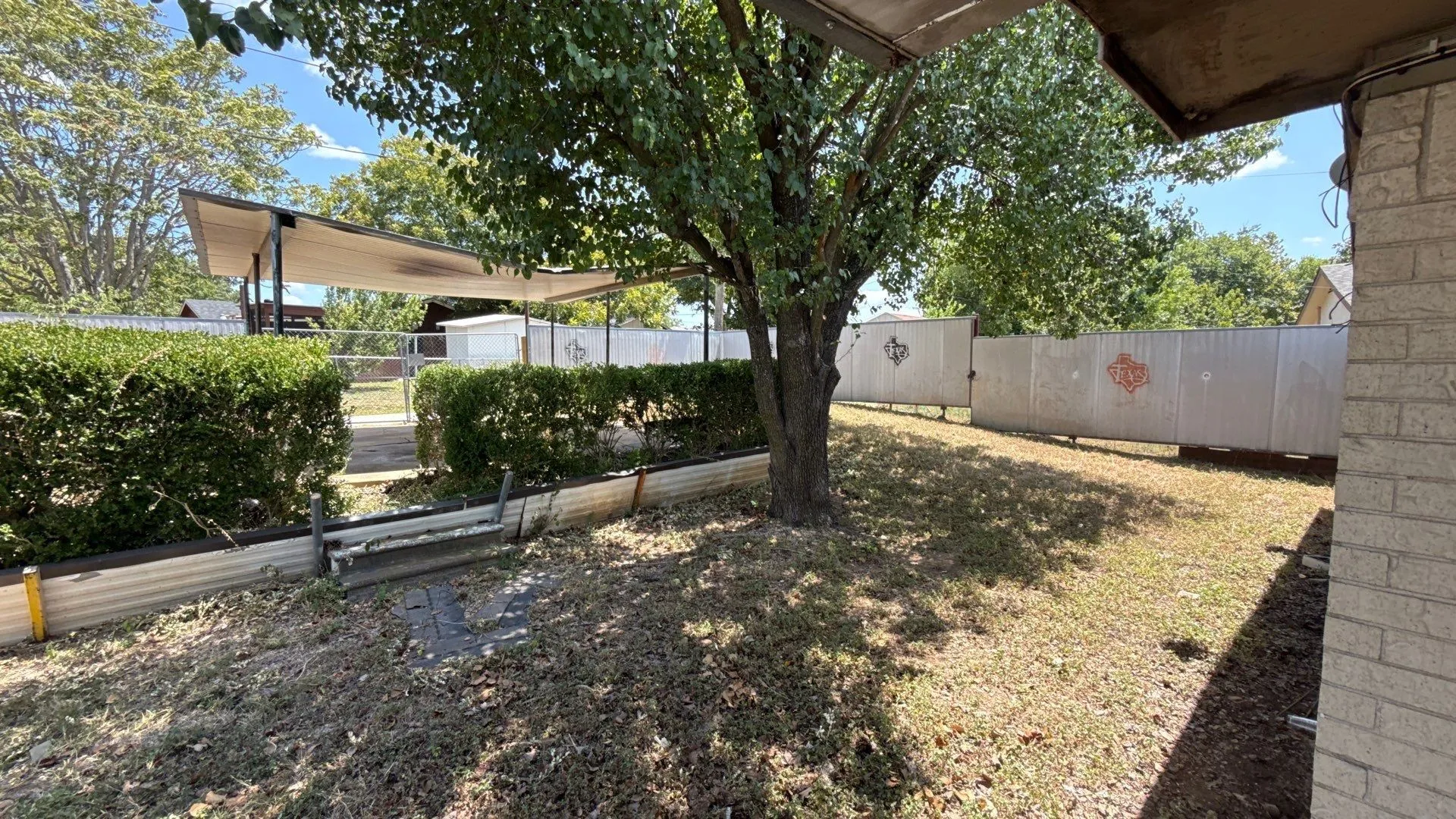 Expansive outdoor space featuring a covered patio, established tree, and low-maintenance landscaping