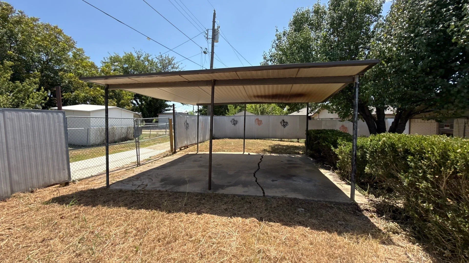 Carport structure with a flat roof, concrete pad, and metal support posts