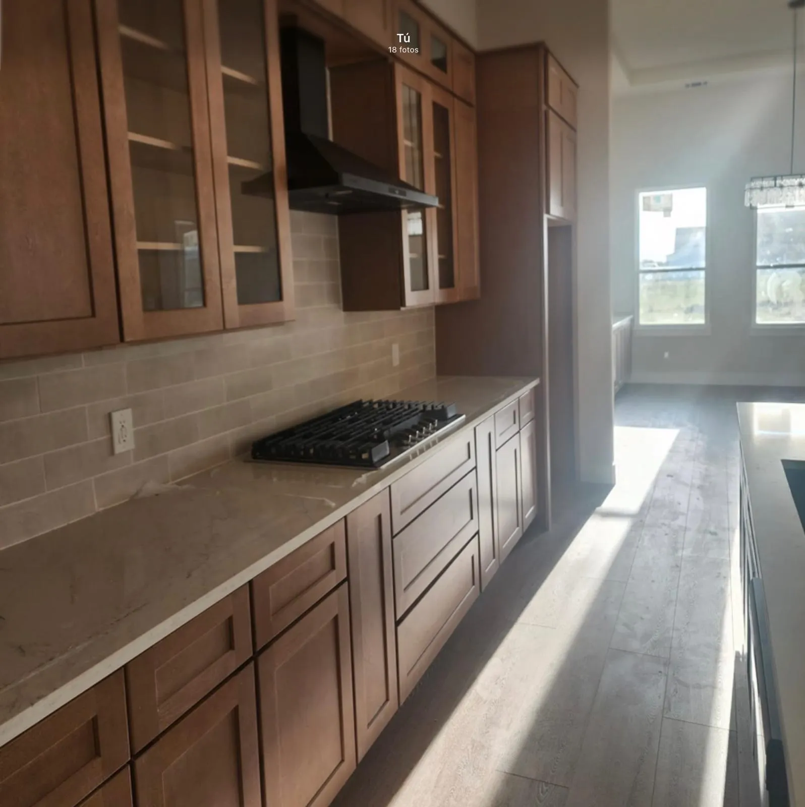Wood-finish flooring, built-in cooktop, neutral tone cabinetry, tile backsplash, and light-colored countertops
