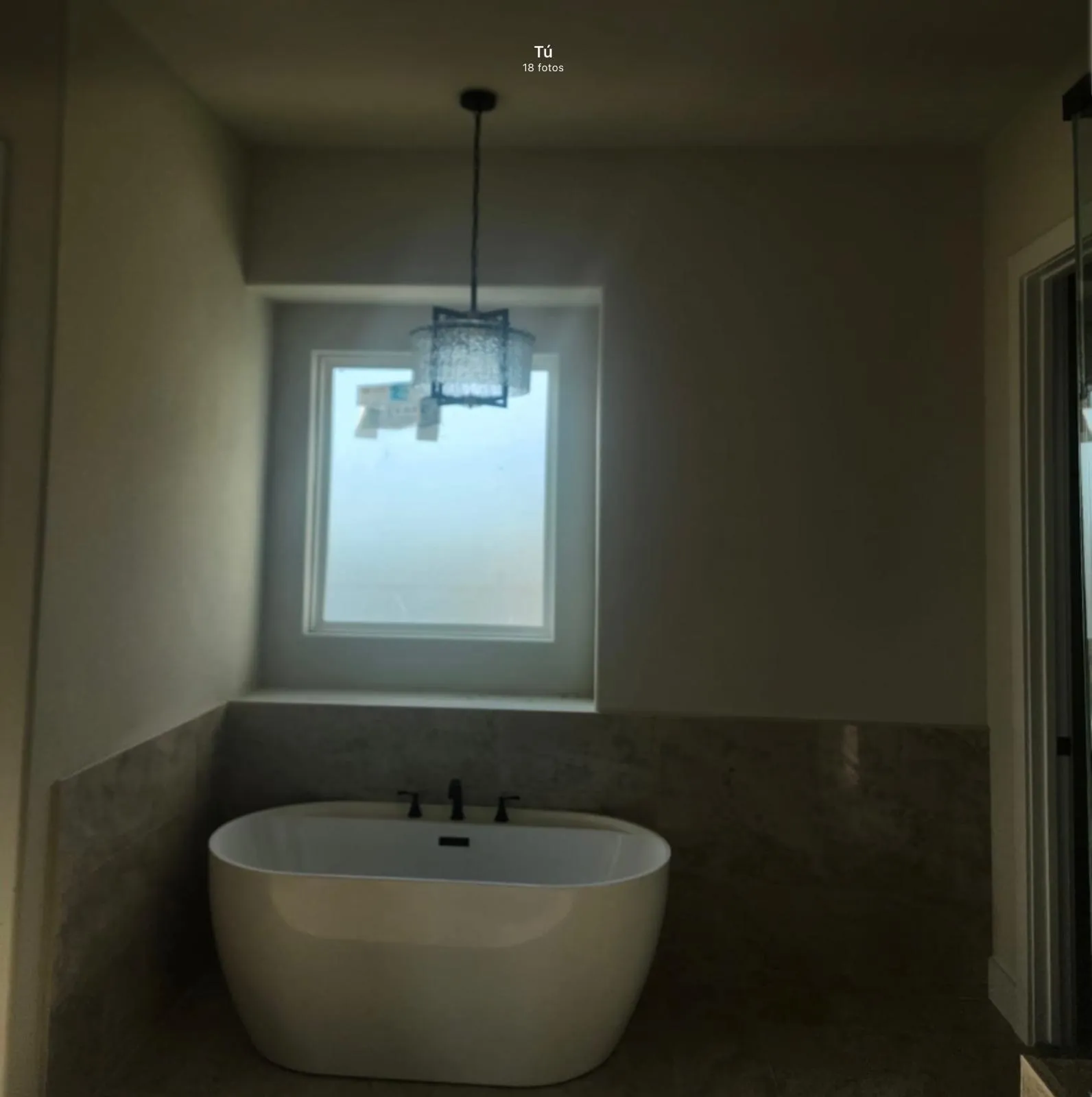 Freestanding soaking tub with dark-toned fixtures, surrounded by floor-to-ceiling tile, illuminated by a decorative pendant light