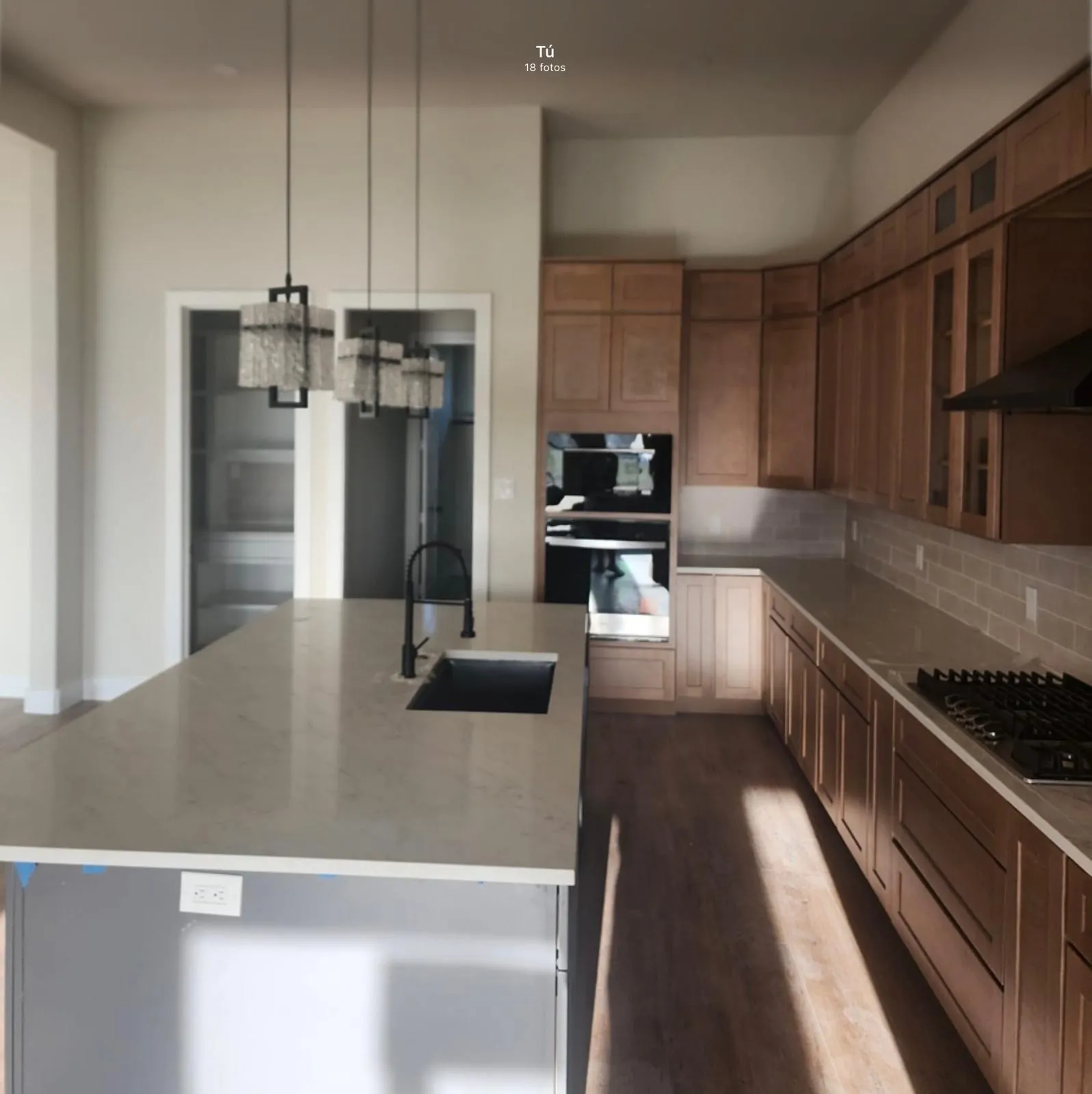 Kitchen featuring an expansive island with an undermount sink, built-in double oven, gas cooktop, wood-finish cabinetry, and tiled backsplash