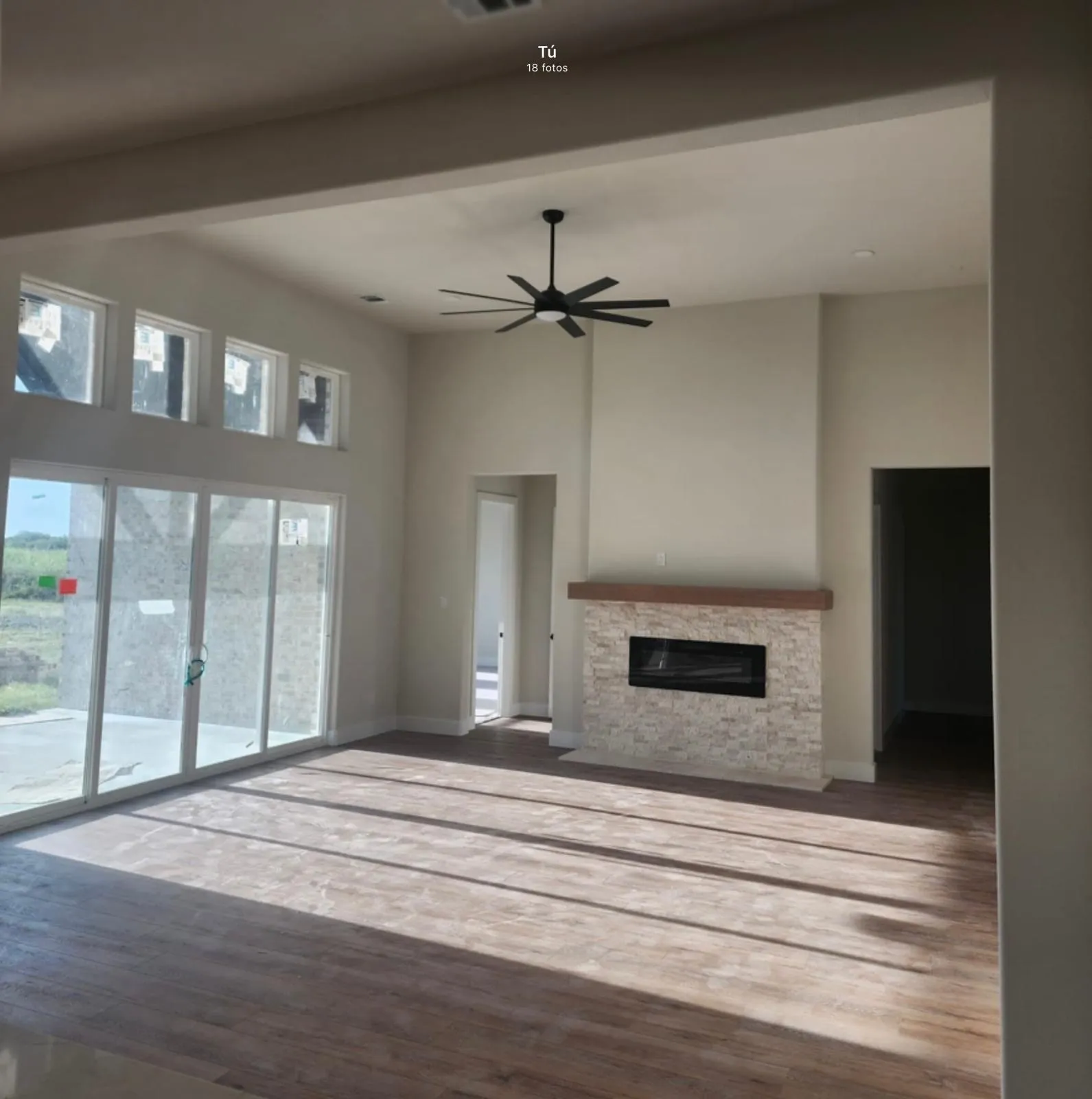 High ceilings featuring a contemporary ceiling fan, wood-finish flooring, a fireplace with a stone surround and wood mantel, and large sliding glass doors