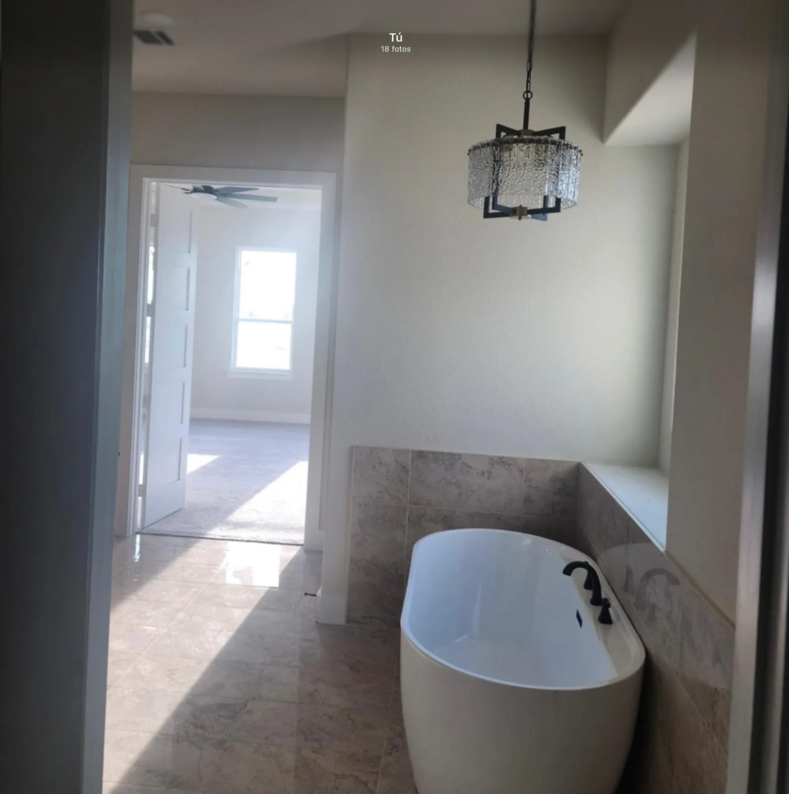 Freestanding soaking tub with matte black fixtures, stone-finish tile surround, and coordinating tile flooring