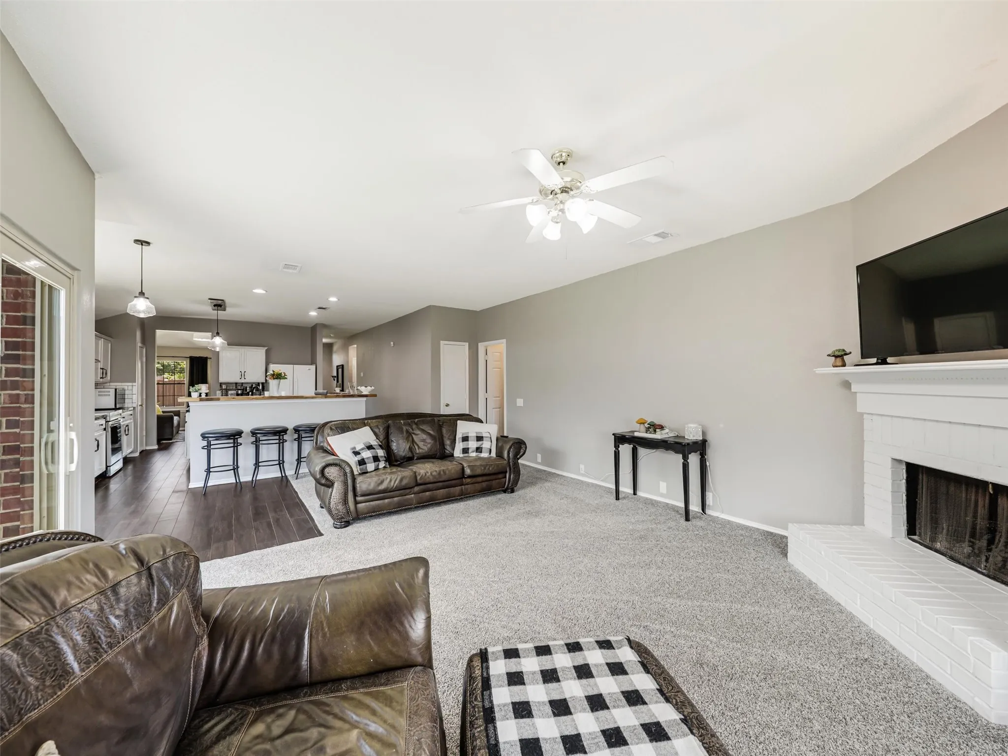 Open-concept living space featuring a fireplace with a white brick hearth, a ceiling fan, and recessed lighting