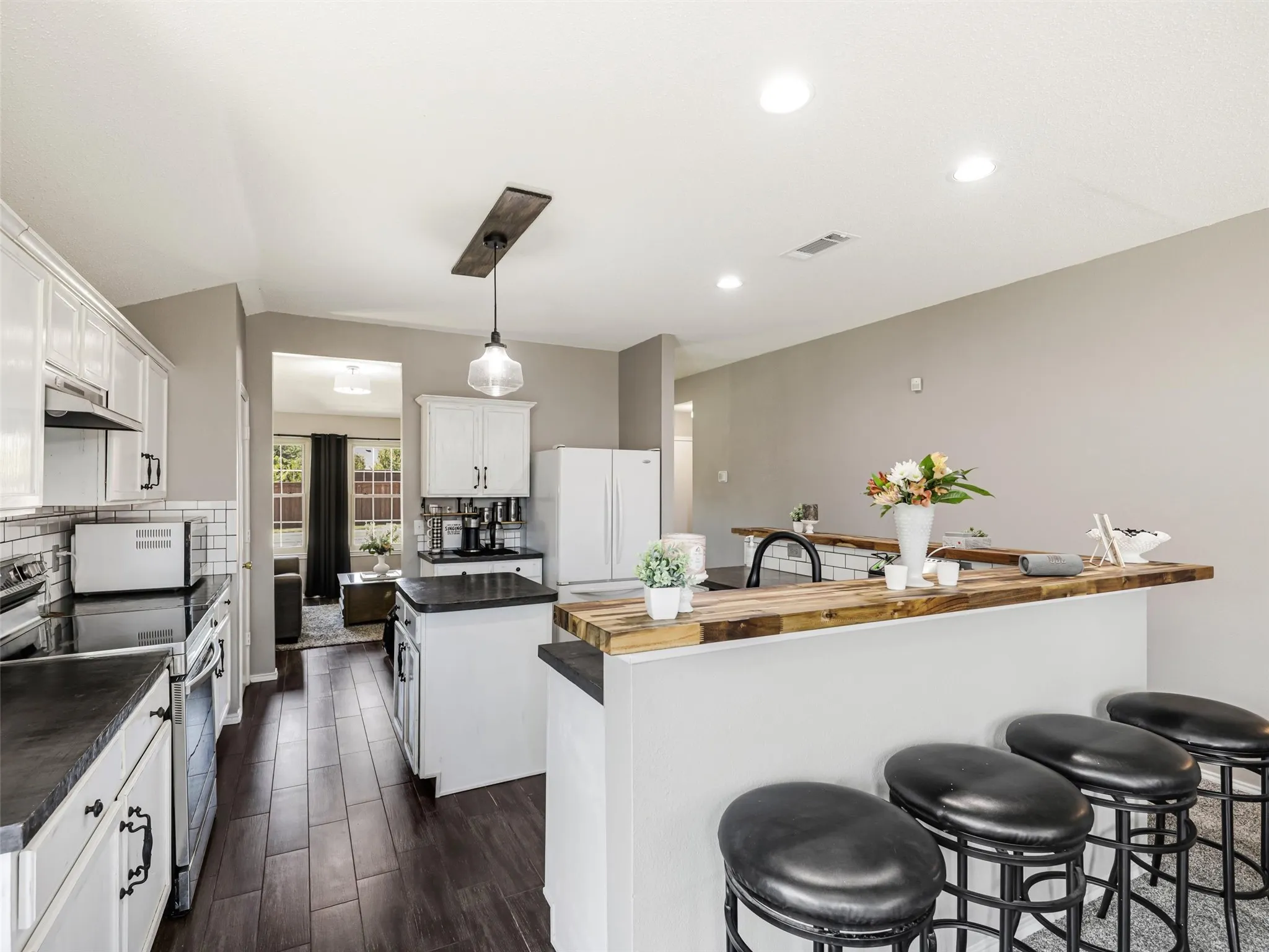Kitchen featuring white cabinetry, dark countertops, a subway tile backsplash, wood-finish flooring, and a breakfast bar with a wood-finish top
