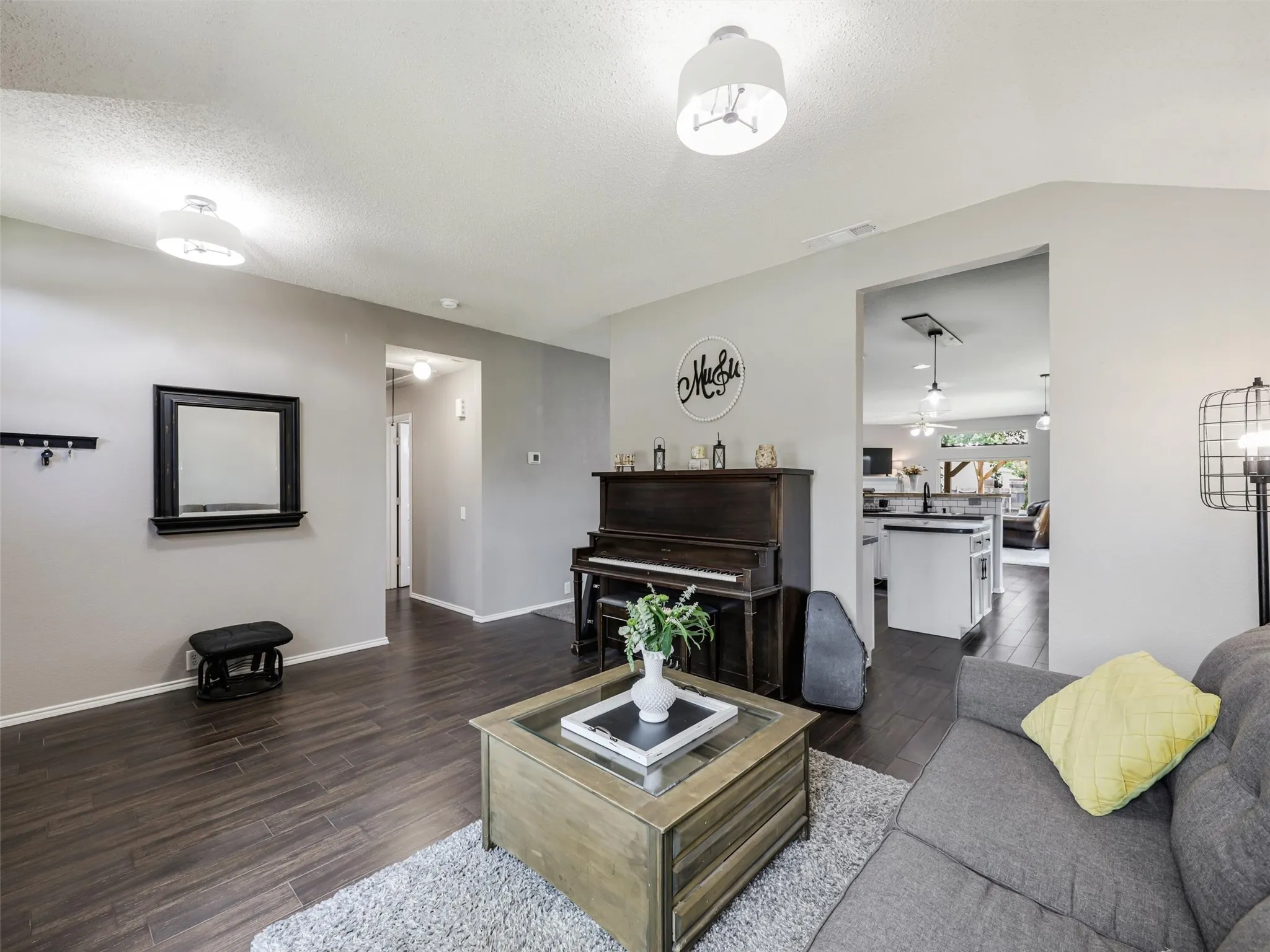 Wood-finish flooring throughout, light gray wall tones, ceiling-mounted light fixtures, and a cased opening leading to an additional area