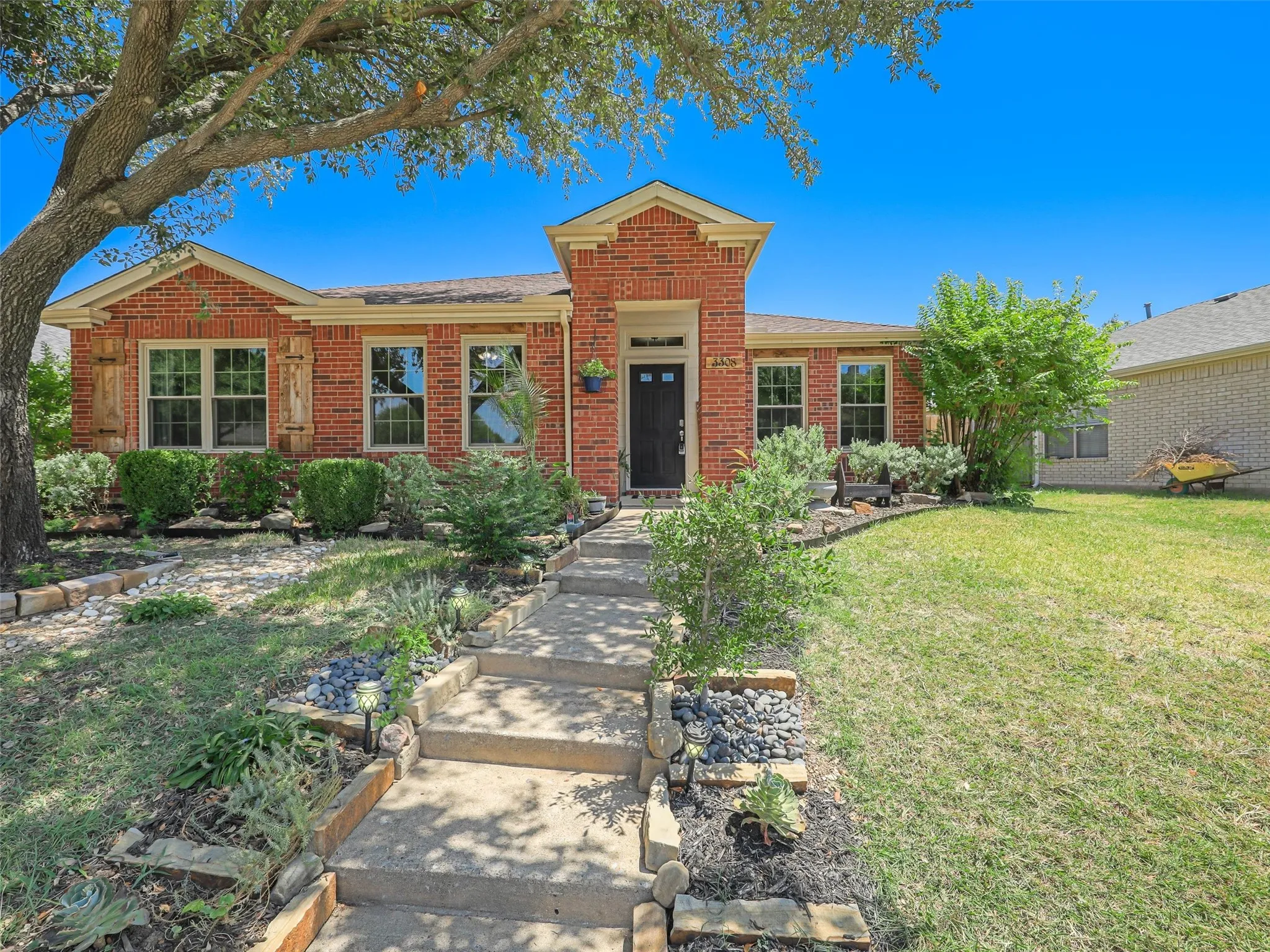 Red brick exterior with a prominent entryway, mature shade tree, and established landscaping