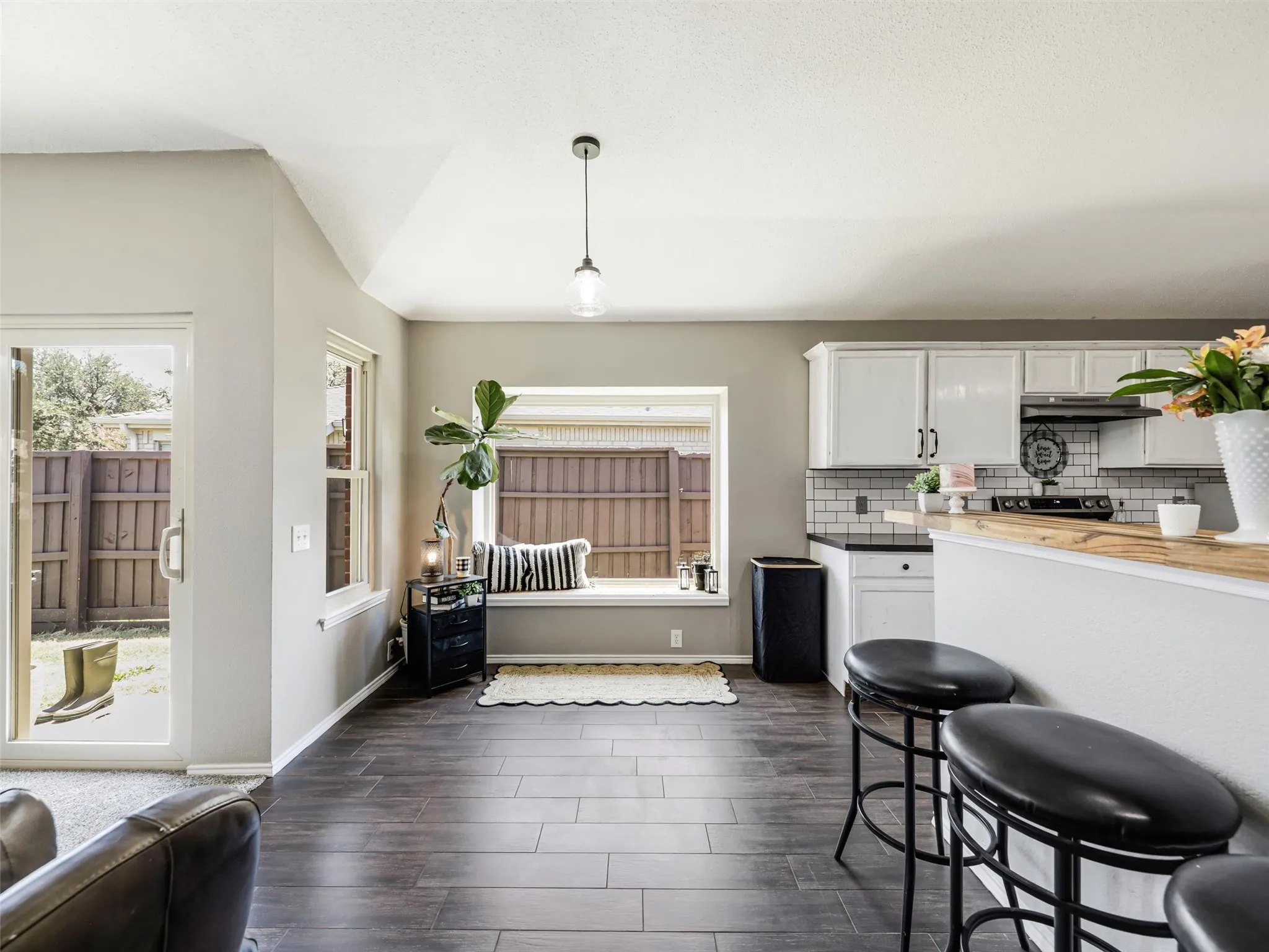 Wood-finish flooring, white cabinetry, subway tile backsplash, built-in window seating, and a glass-paneled patio door