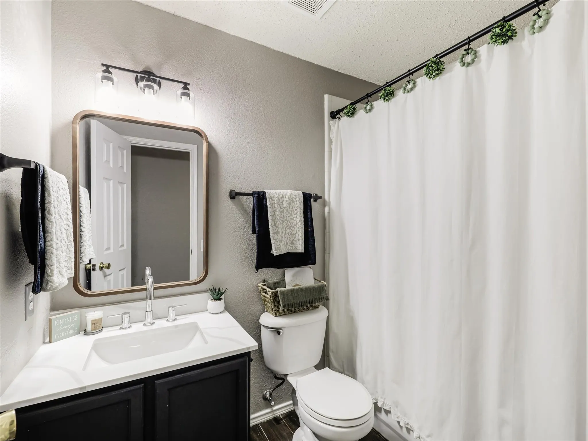 Vanity with white countertop and black cabinetry, rectangular mirror, and a three-light vanity fixture