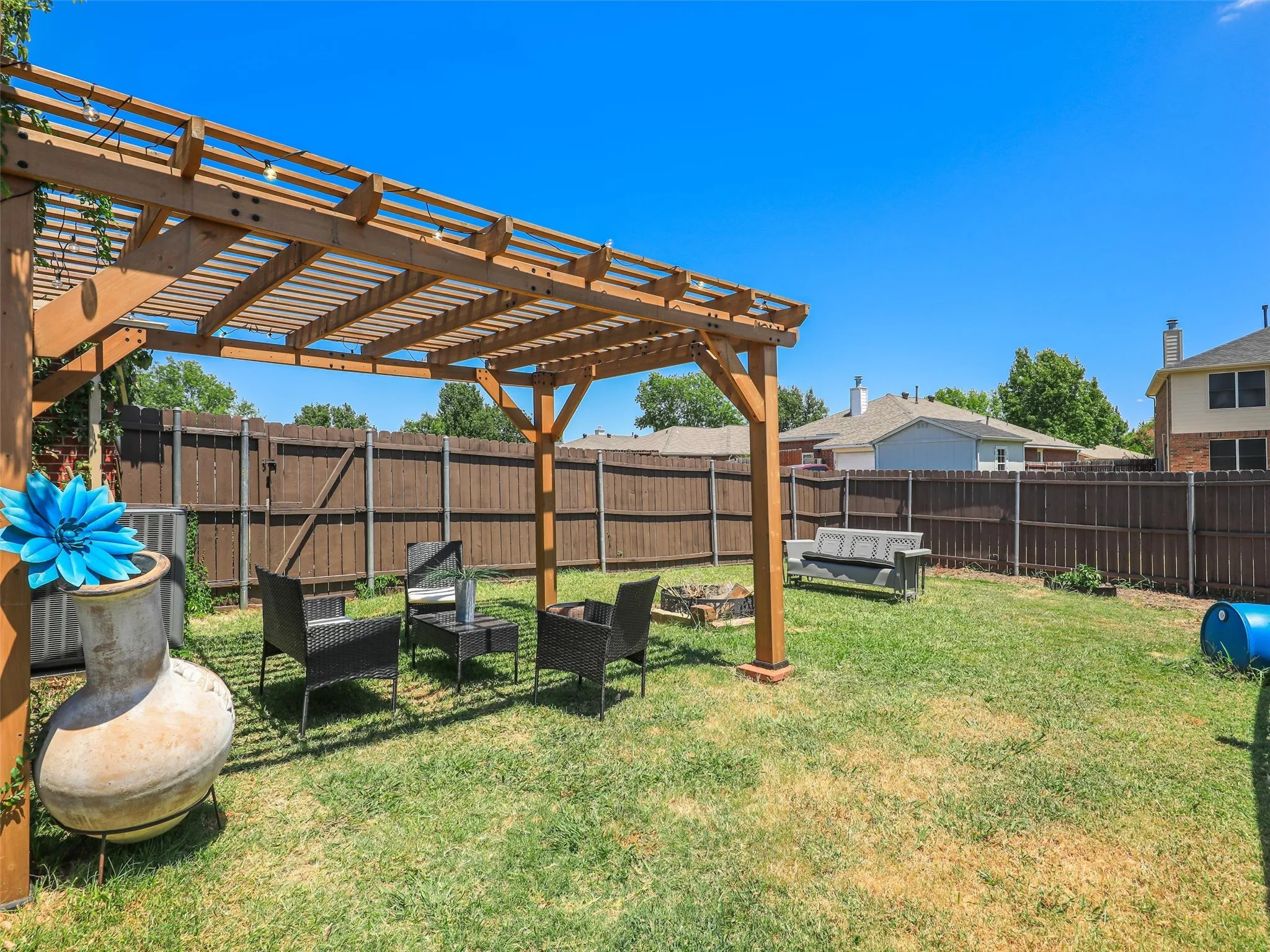 Expansive backyard featuring a wood pergola with a translucent roof, a dedicated fire pit area, and a privacy fence