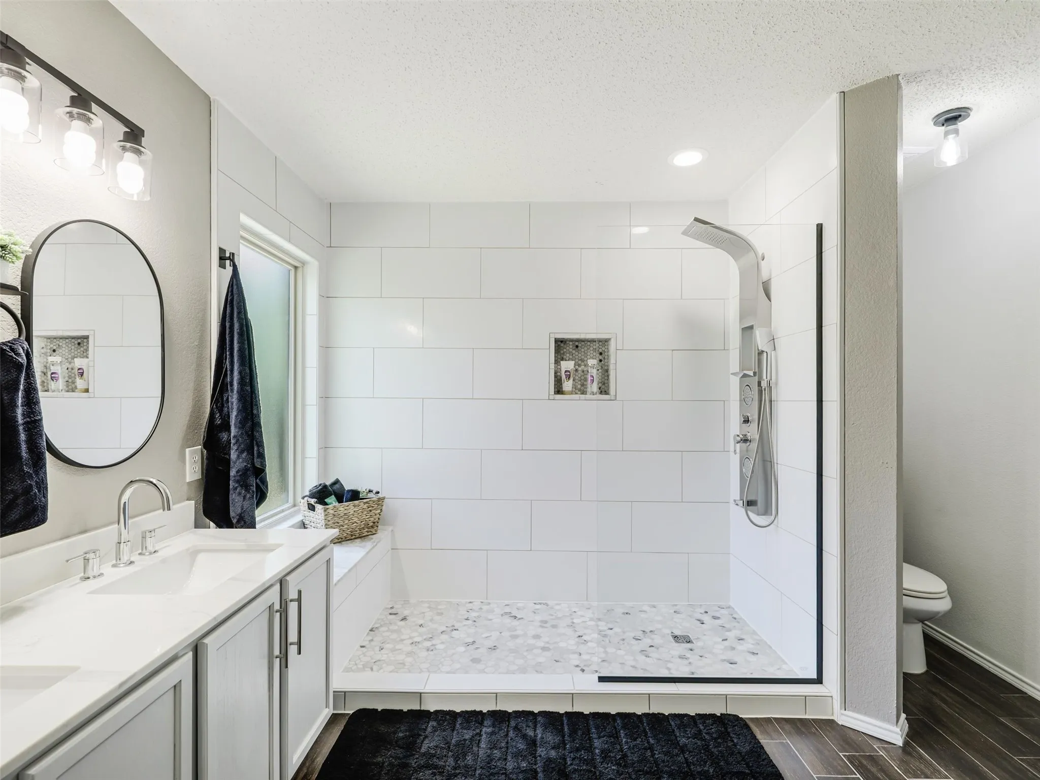 Spacious bathroom featuring a double vanity with ample counter space, a walk-in shower with white subway tile, a recessed shower niche, and wood-finish flooring